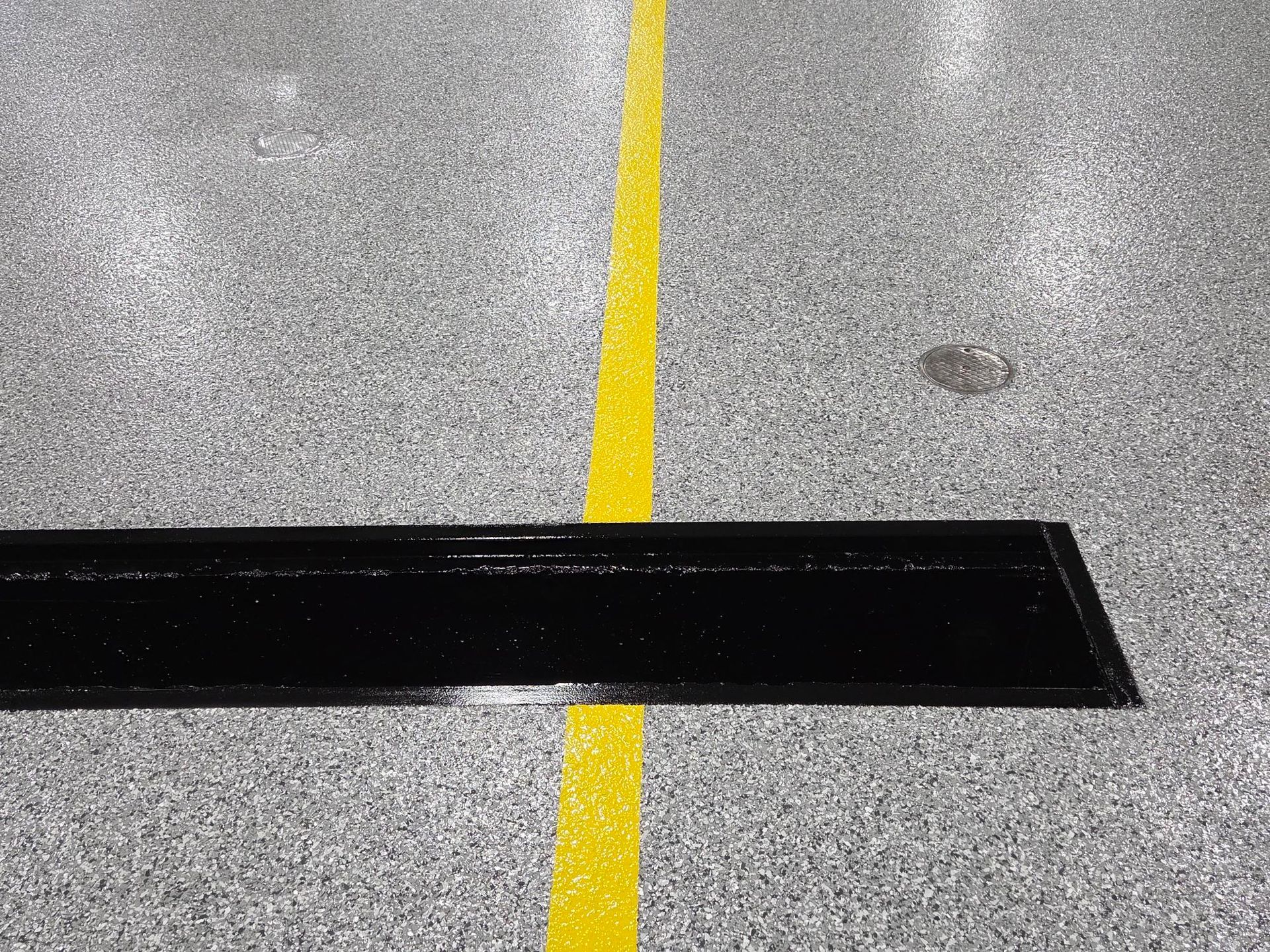 Yellow line on gray pavement crossing a black speed bump strip