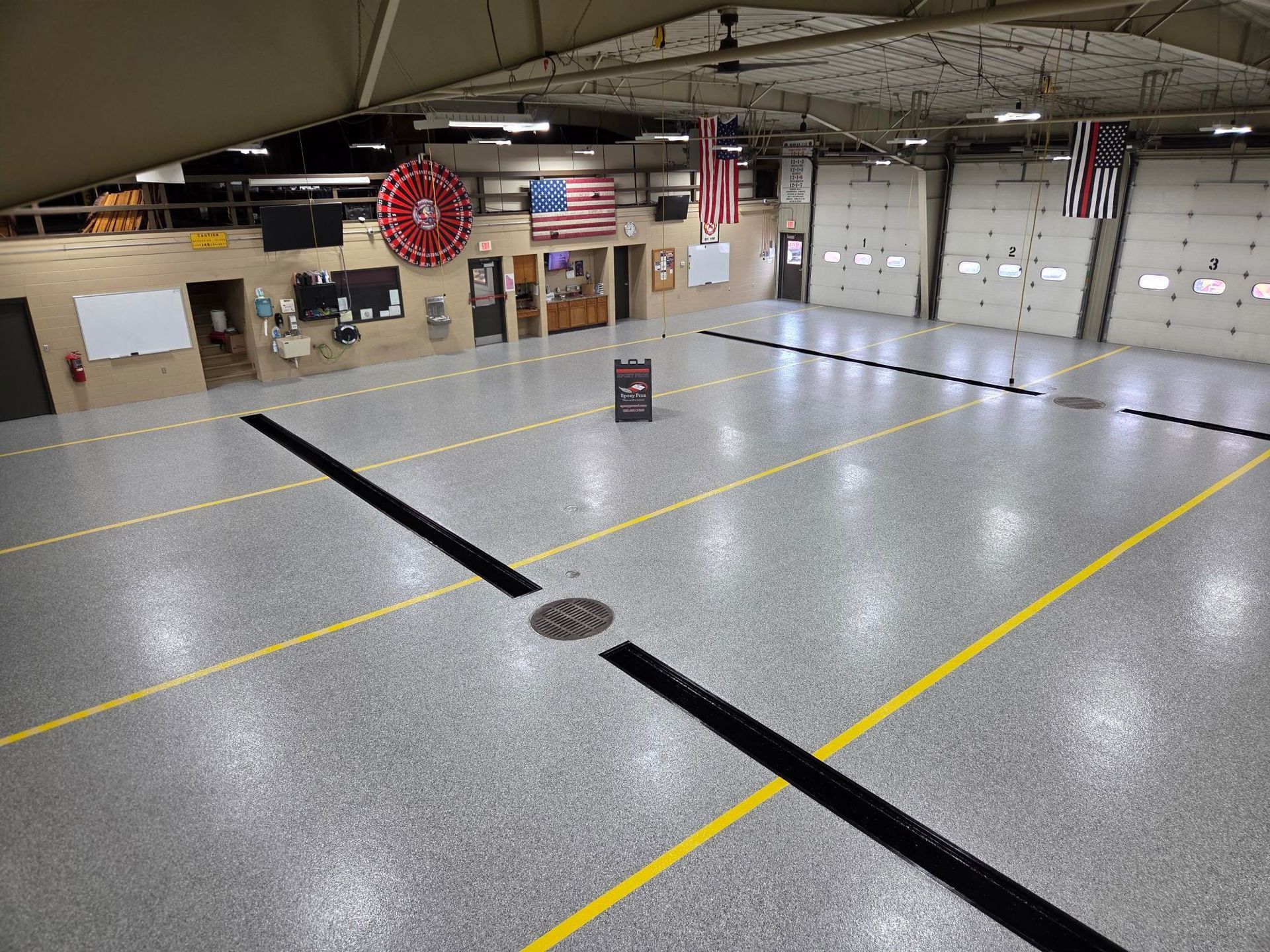 Empty indoor sports court with yellow lines, black floor strips, and flags hanging from the ceiling