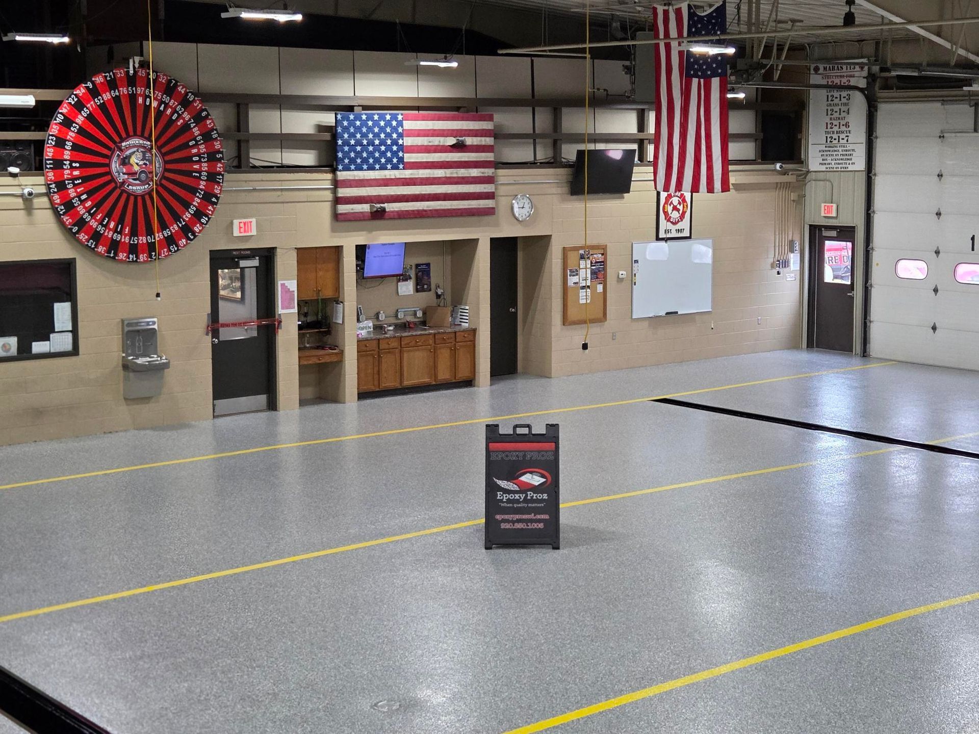 Empty gym with hanging flags, a large red wall fan, and a folding sign on the floor.