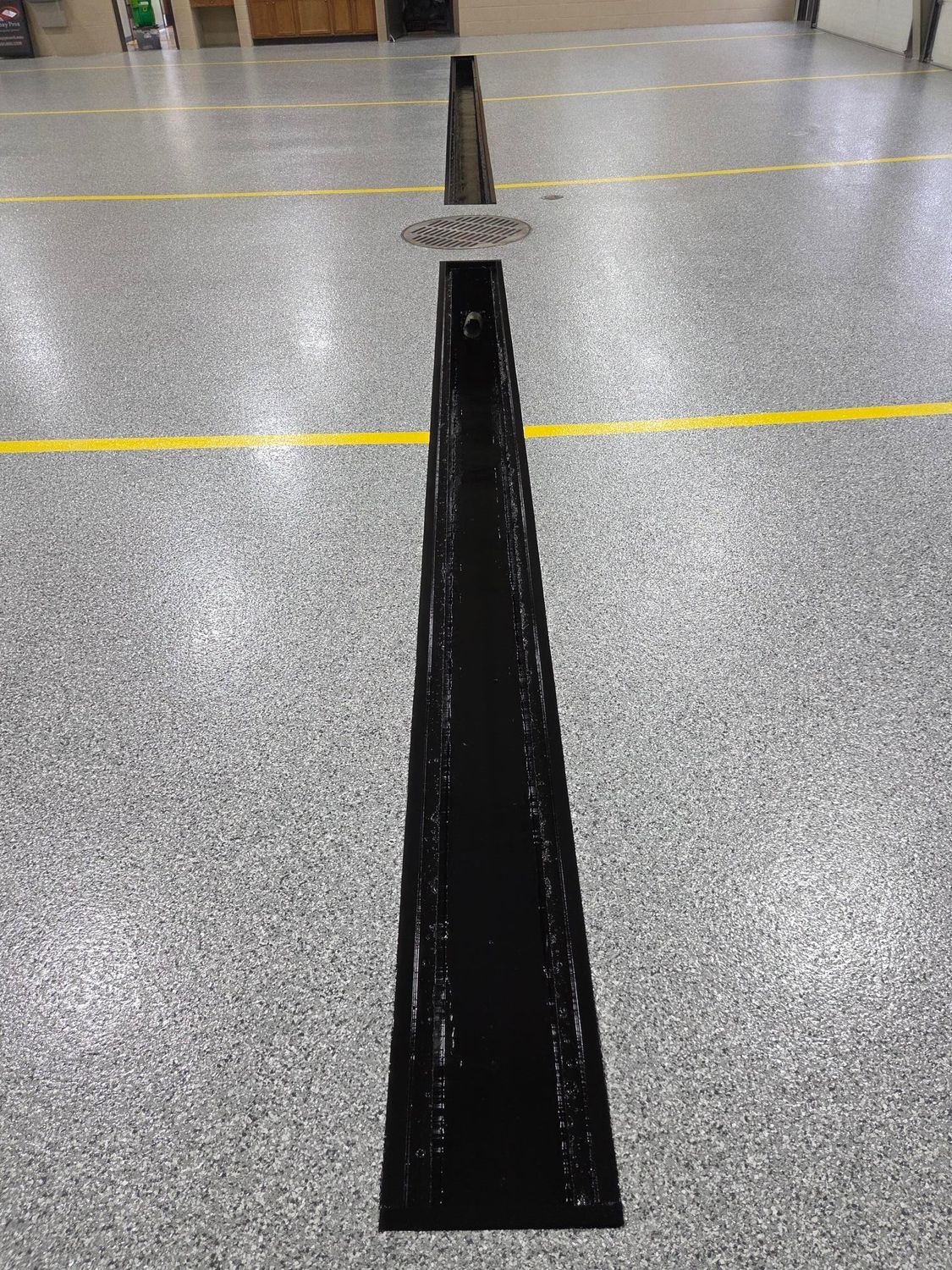 Long black tape strip on a speckled floor, leading toward a small cone in the distance.