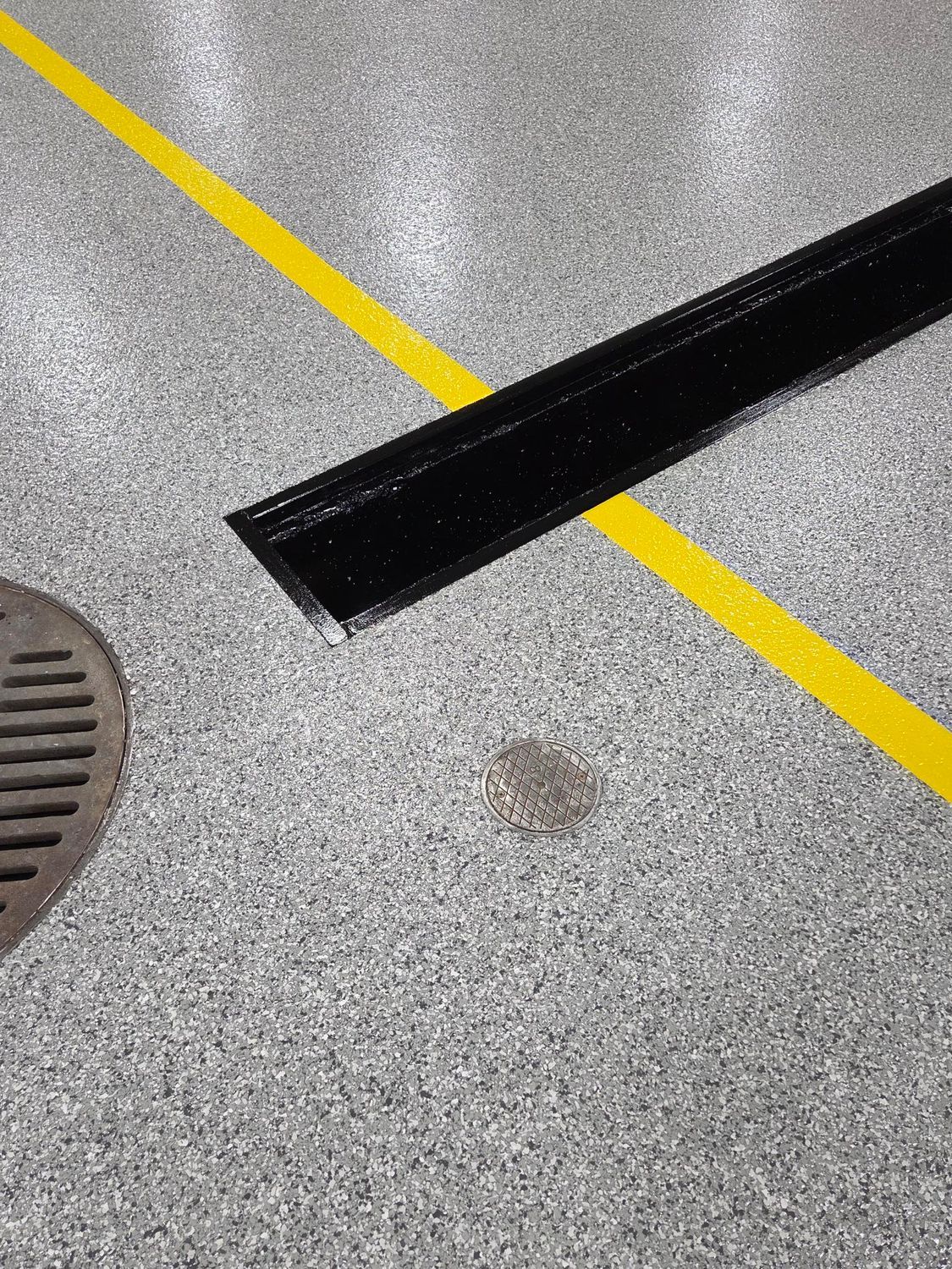 Gray speckled floor with a yellow line, black metal strip, drain grate, and a small stain