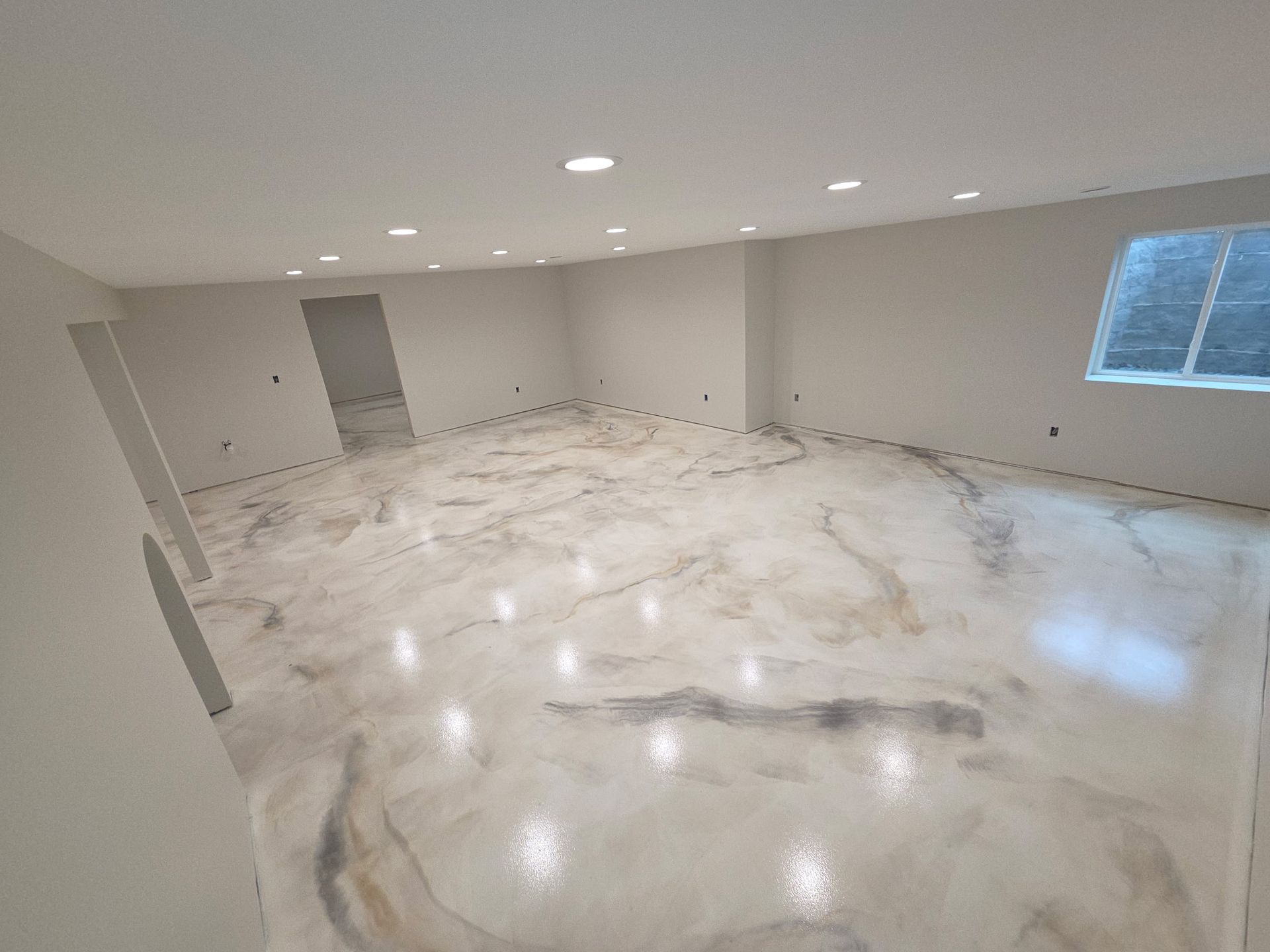 Empty unfinished room with glossy concrete floor, recessed lights, and a small window
