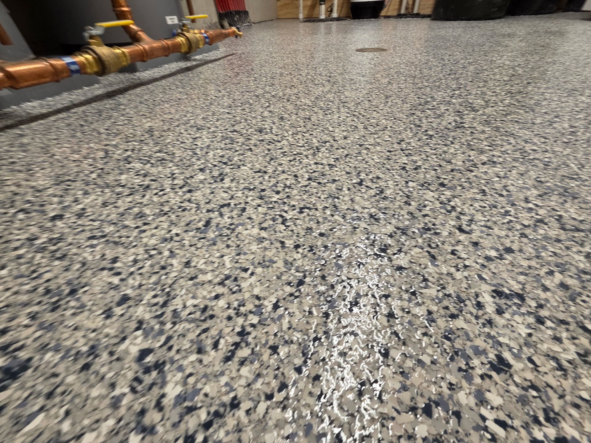 Speckled gray epoxy floor in an industrial room with pipes along the wall