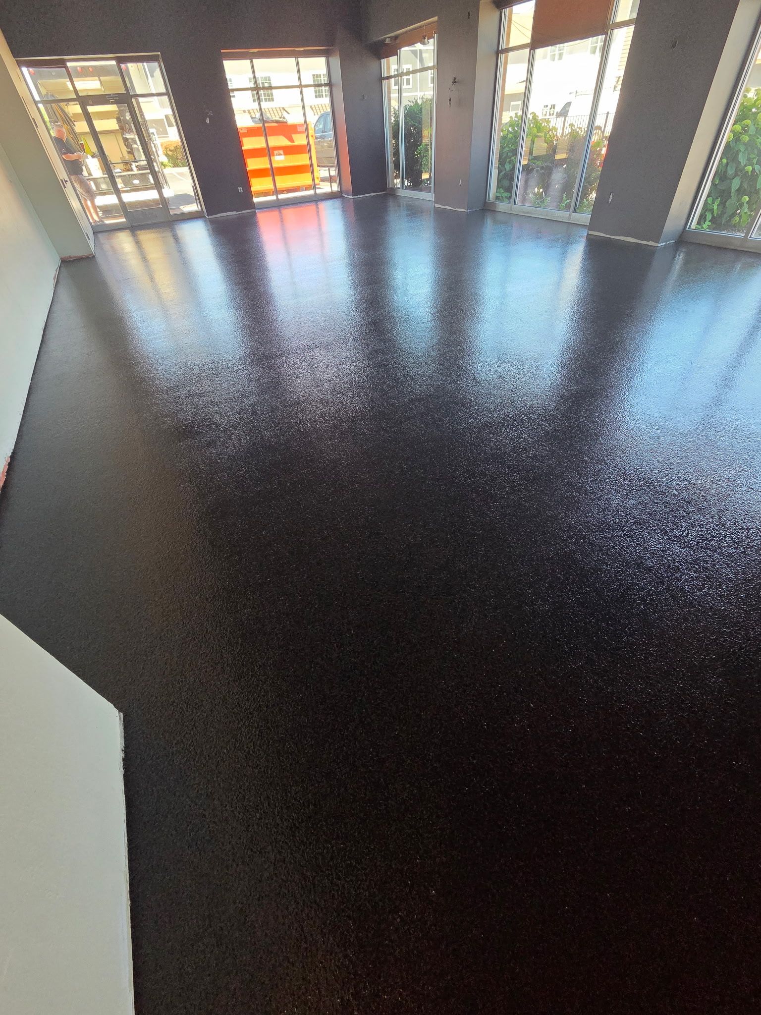 Empty room with glossy dark floor and large windows letting in daylight