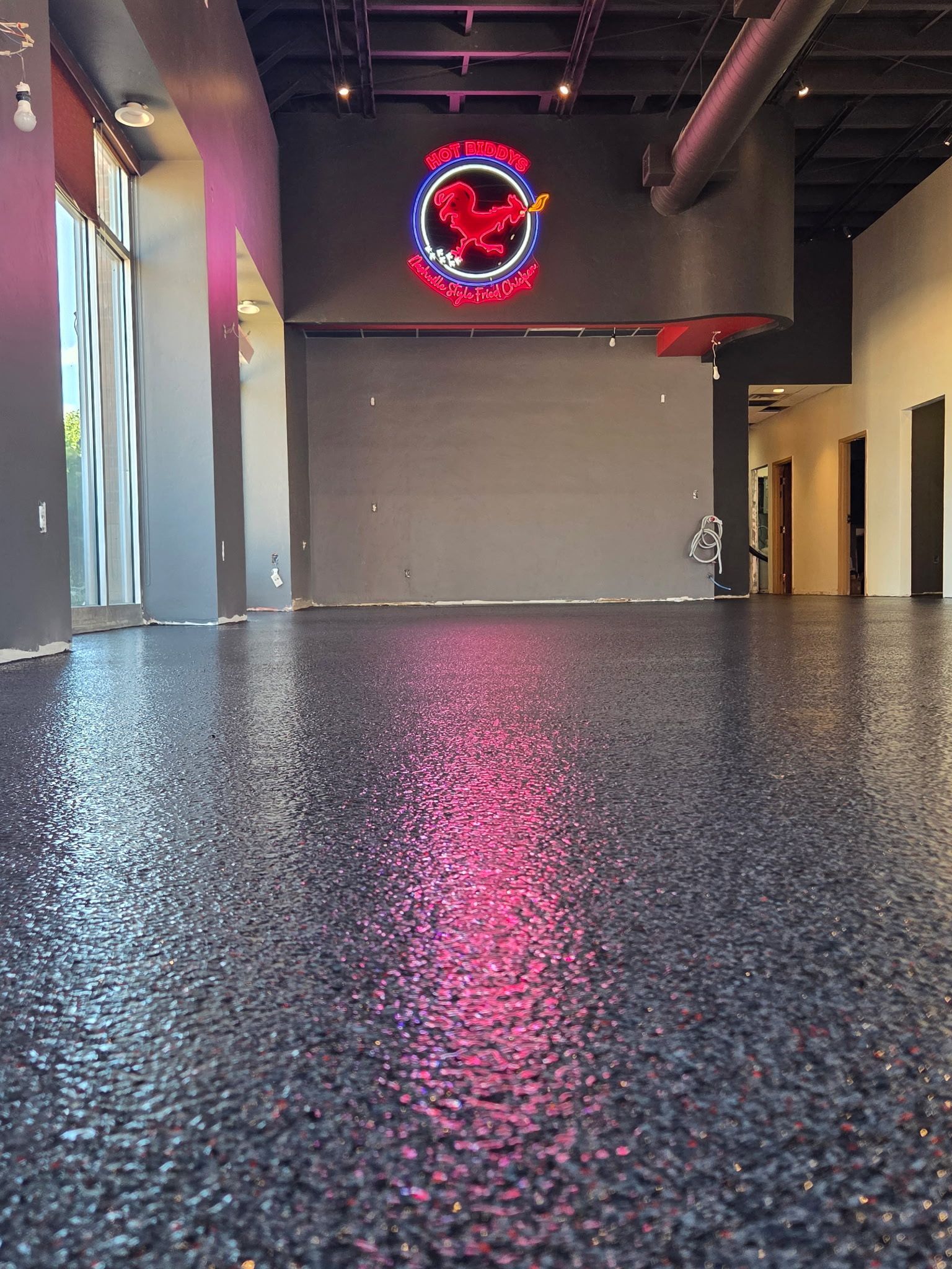 Empty modern lobby with glossy black floor, red neon wall sign, and doorway at right.