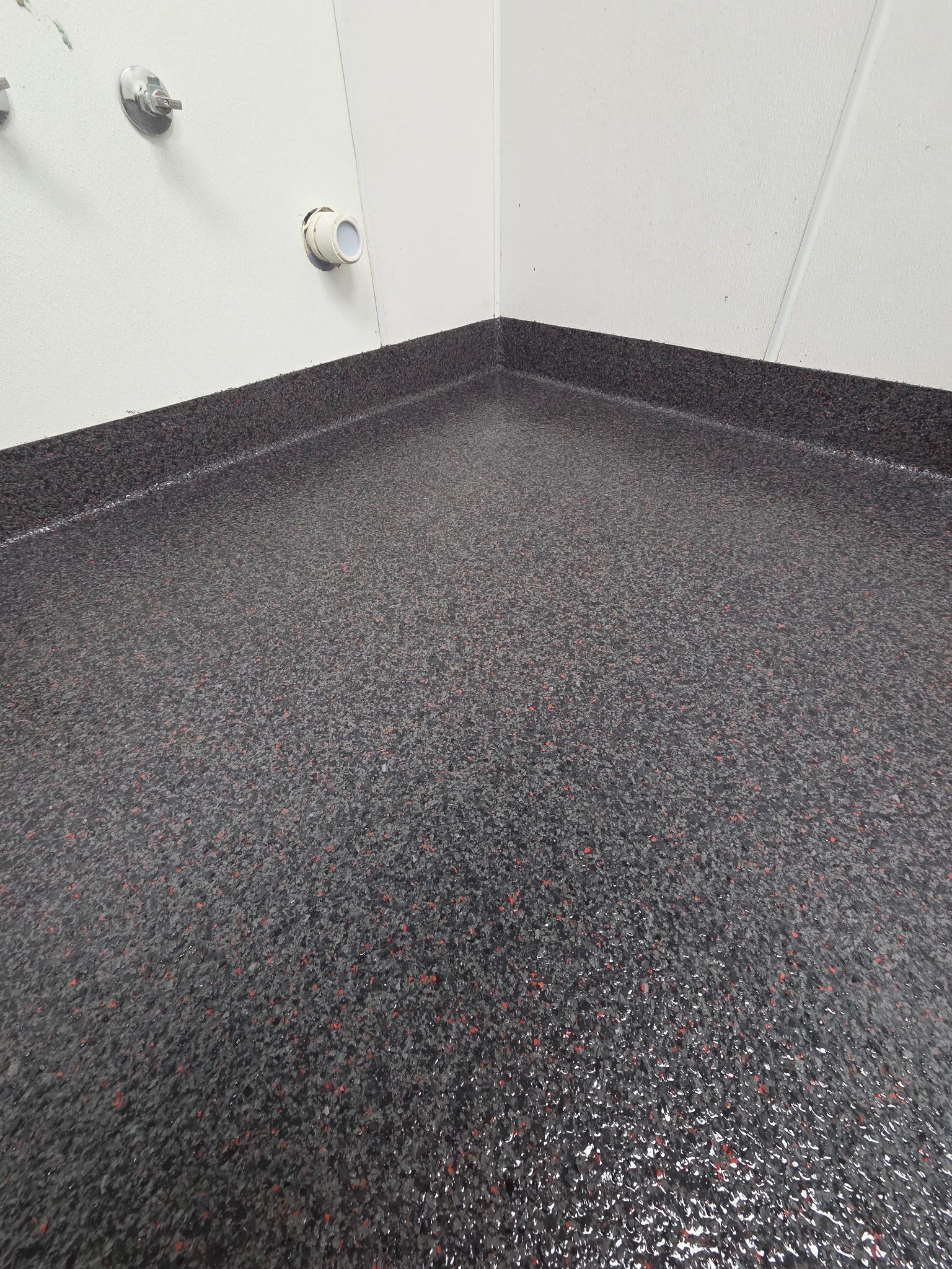 Empty corner of a room with dark speckled flooring and white walls with outlets.