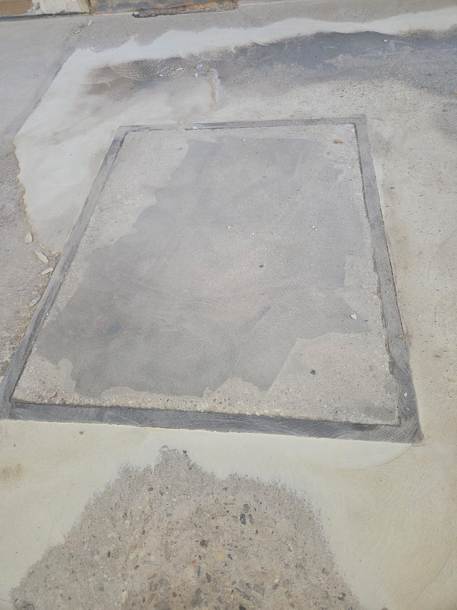 Concrete pavement with a square utility cover patch and surrounding damaged asphalt.