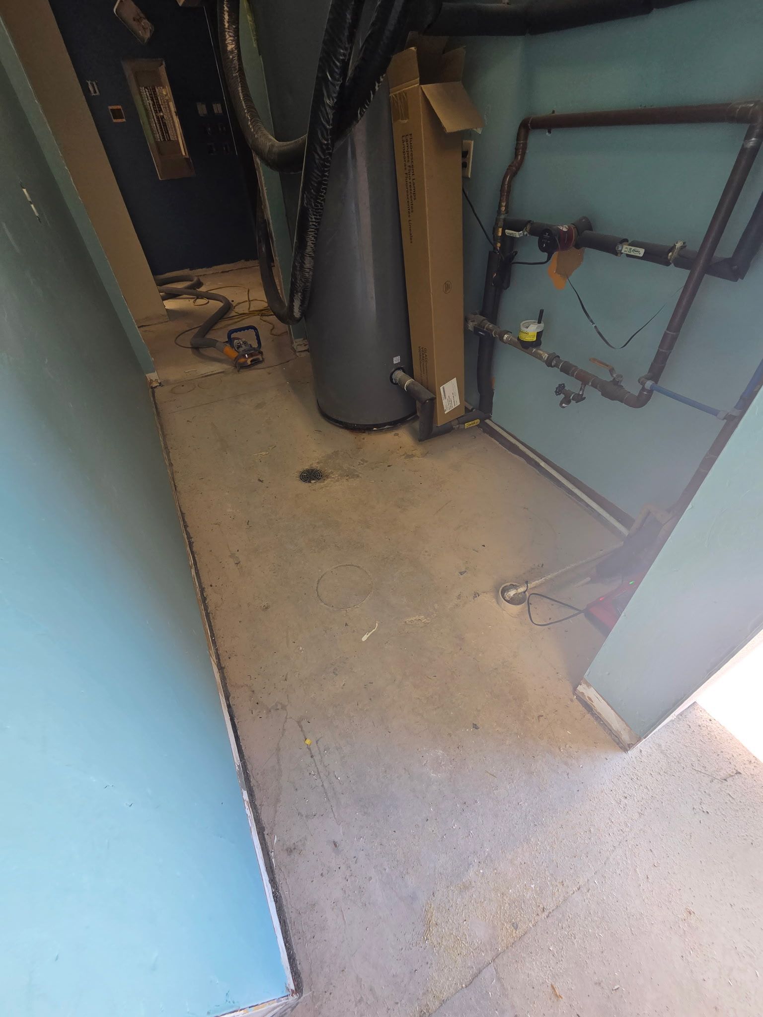 Dim utility room with blue doors, exposed pipes, and a water heater on a concrete floor.