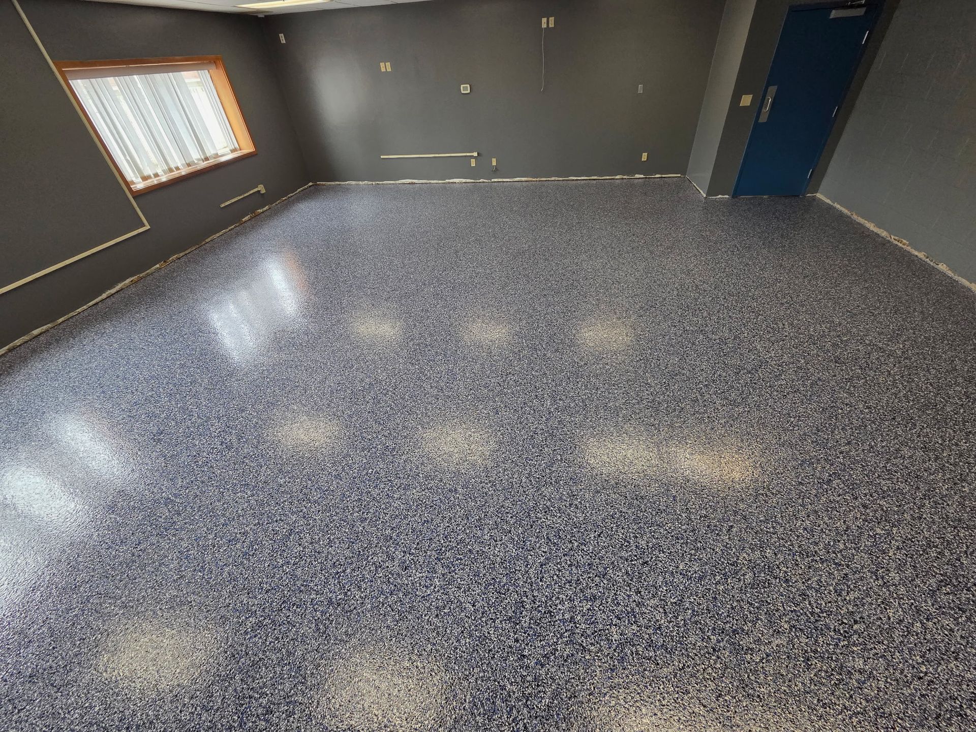 Empty room with dark gray walls, speckled floor, a window, and a blue door.
