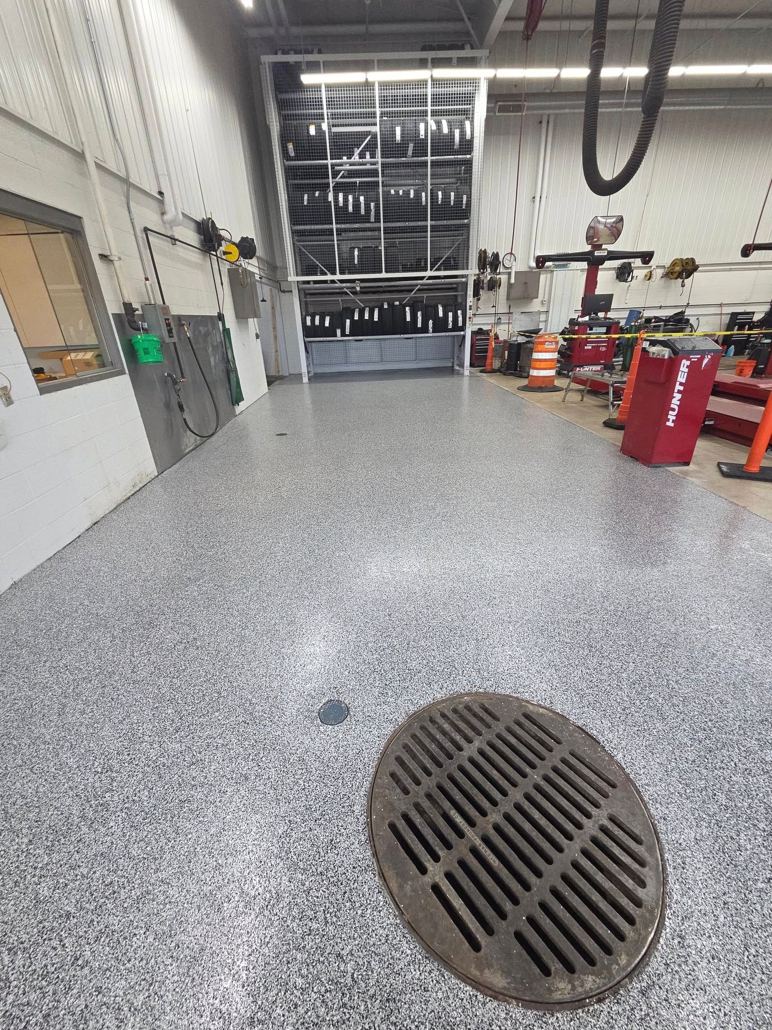 A gray speckled industrial floor with a drain cover, leading to a bay door.