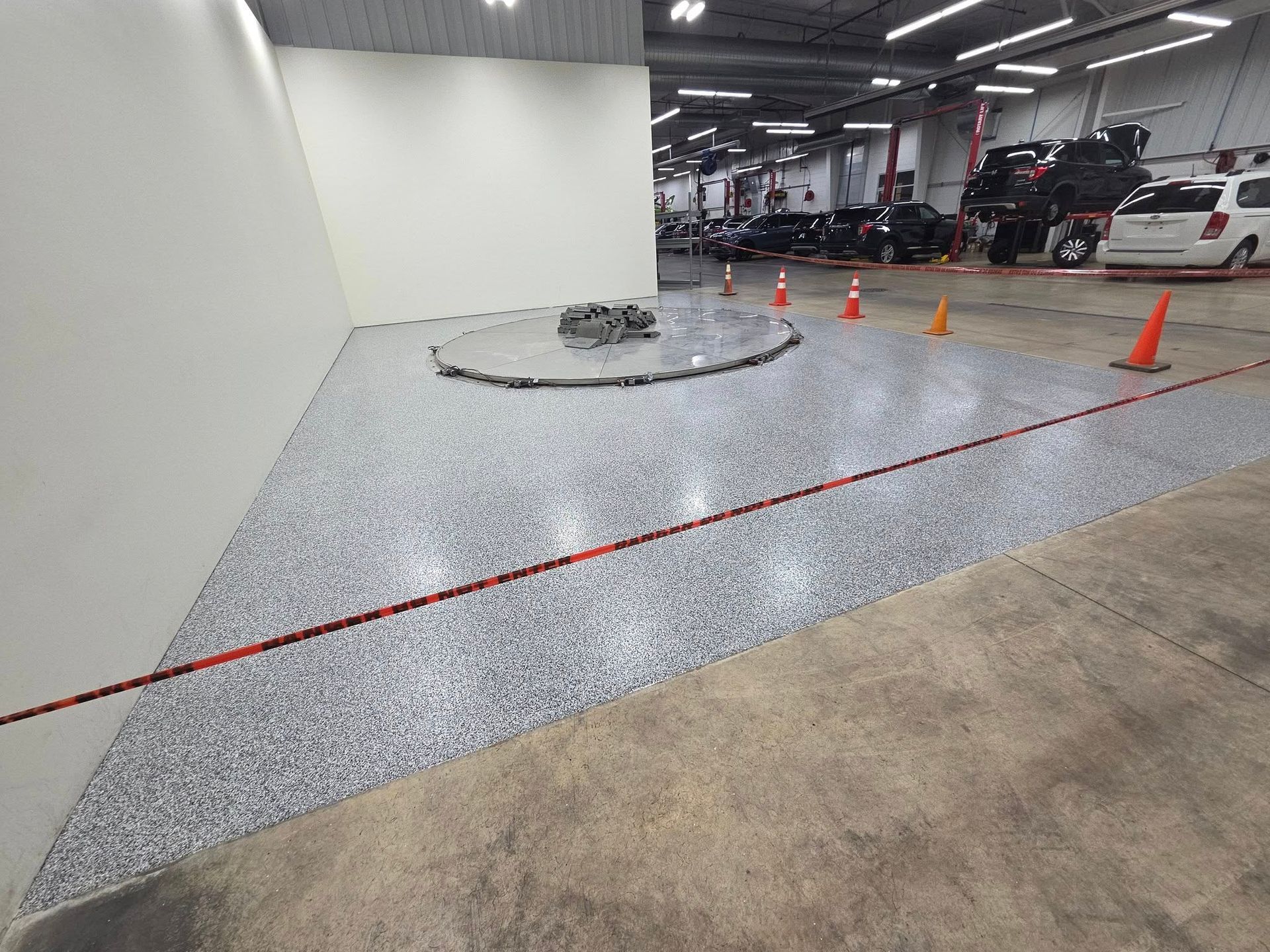 Triangular floor with speckled gray finish, surrounded by a red rope and orange cones in a large garage setting.