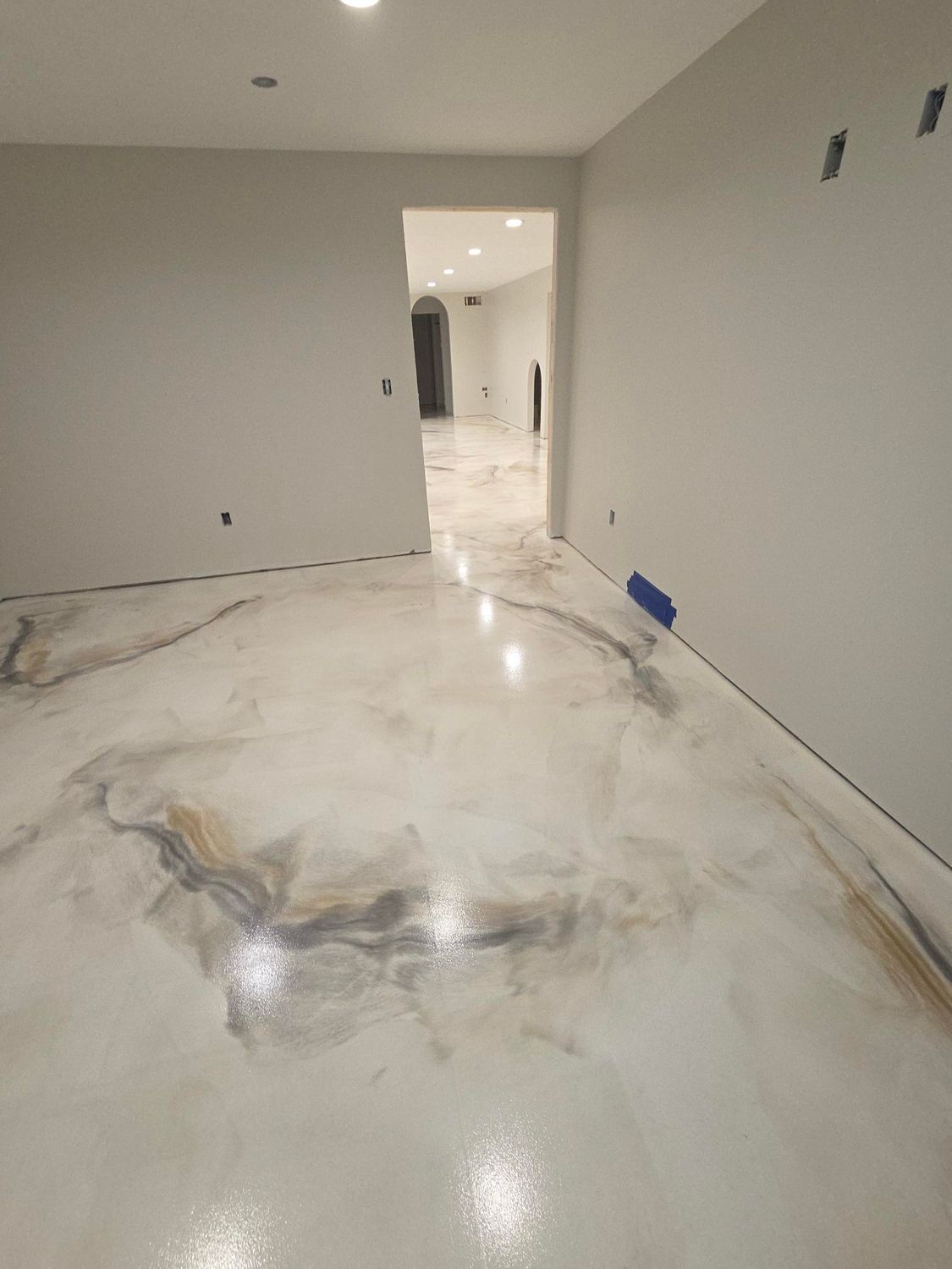 A modern room with a glossy, white-and-gray marbled epoxy floor leading to a hallway with recessed lighting