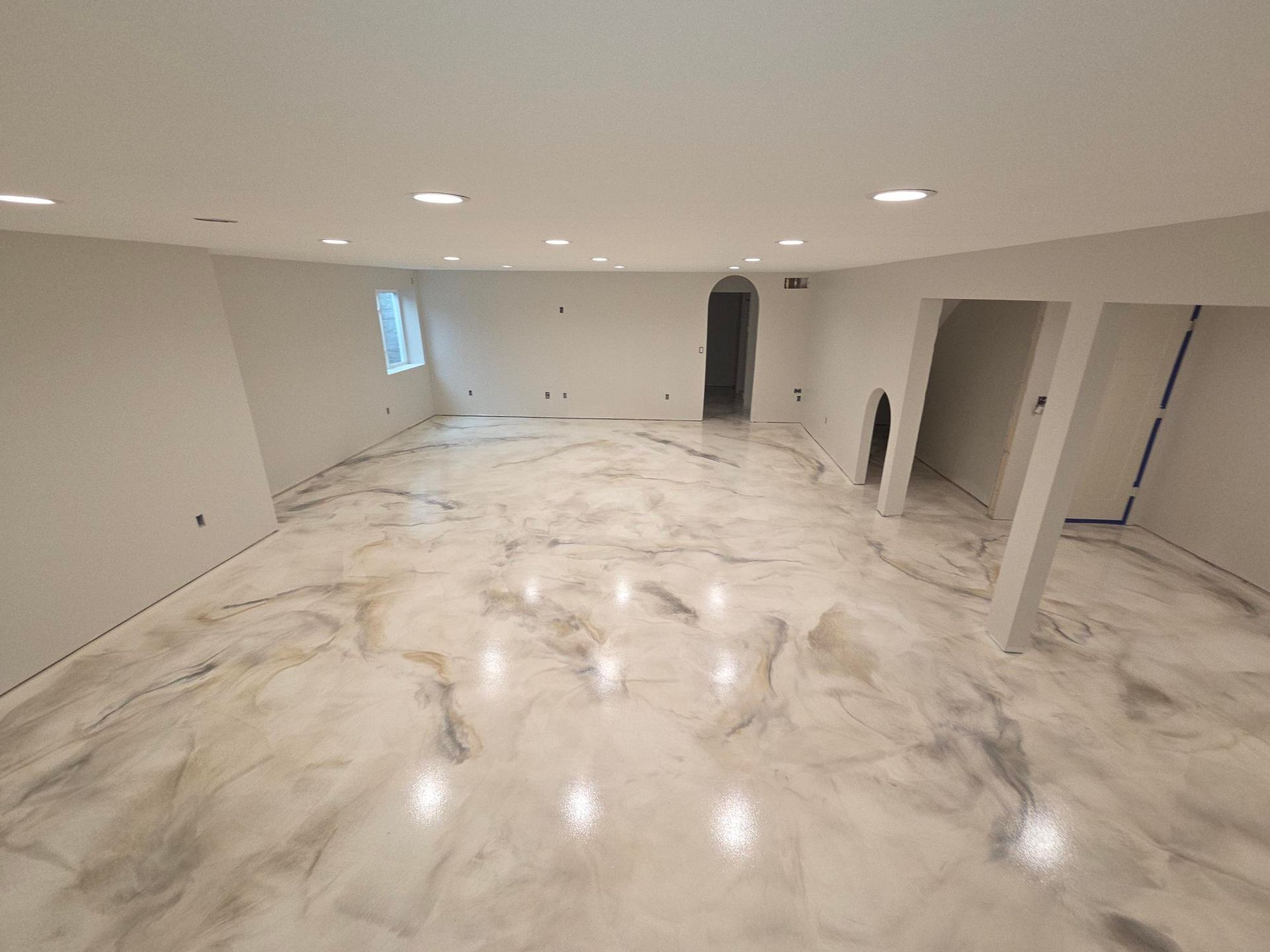 A wide, empty room features a glossy, white and grey marble-patterned epoxy floor with recessed ceiling lighting