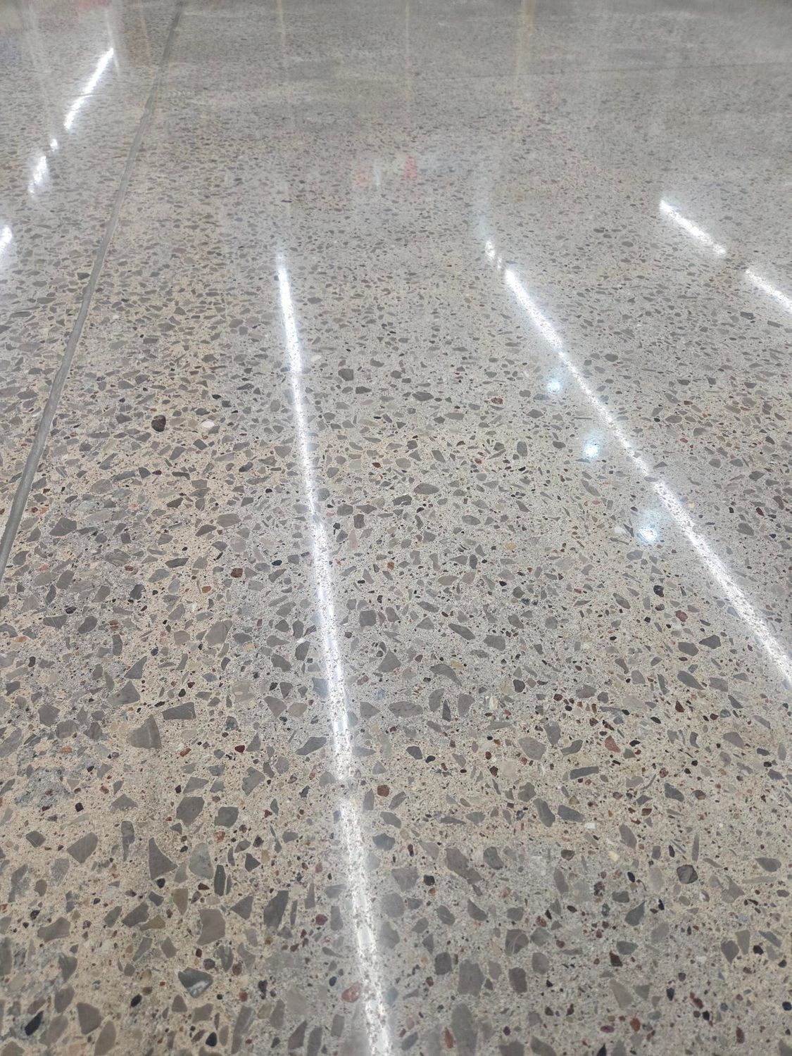 A polished concrete floor with exposed aggregate, featuring light reflections from overhead lighting