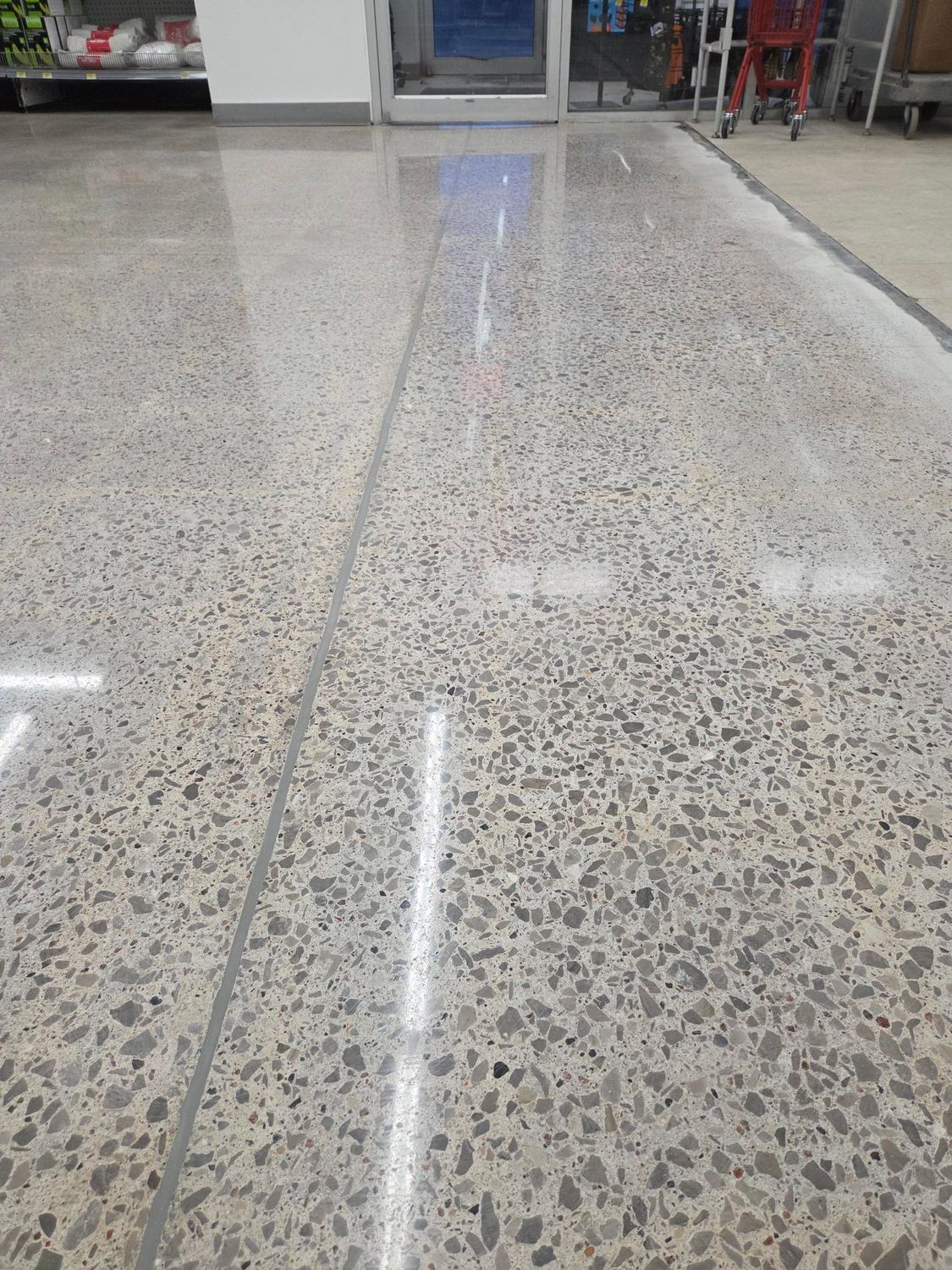 Polished, light-colored concrete flooring with a speckled aggregate texture, featuring a straight seam running vertically