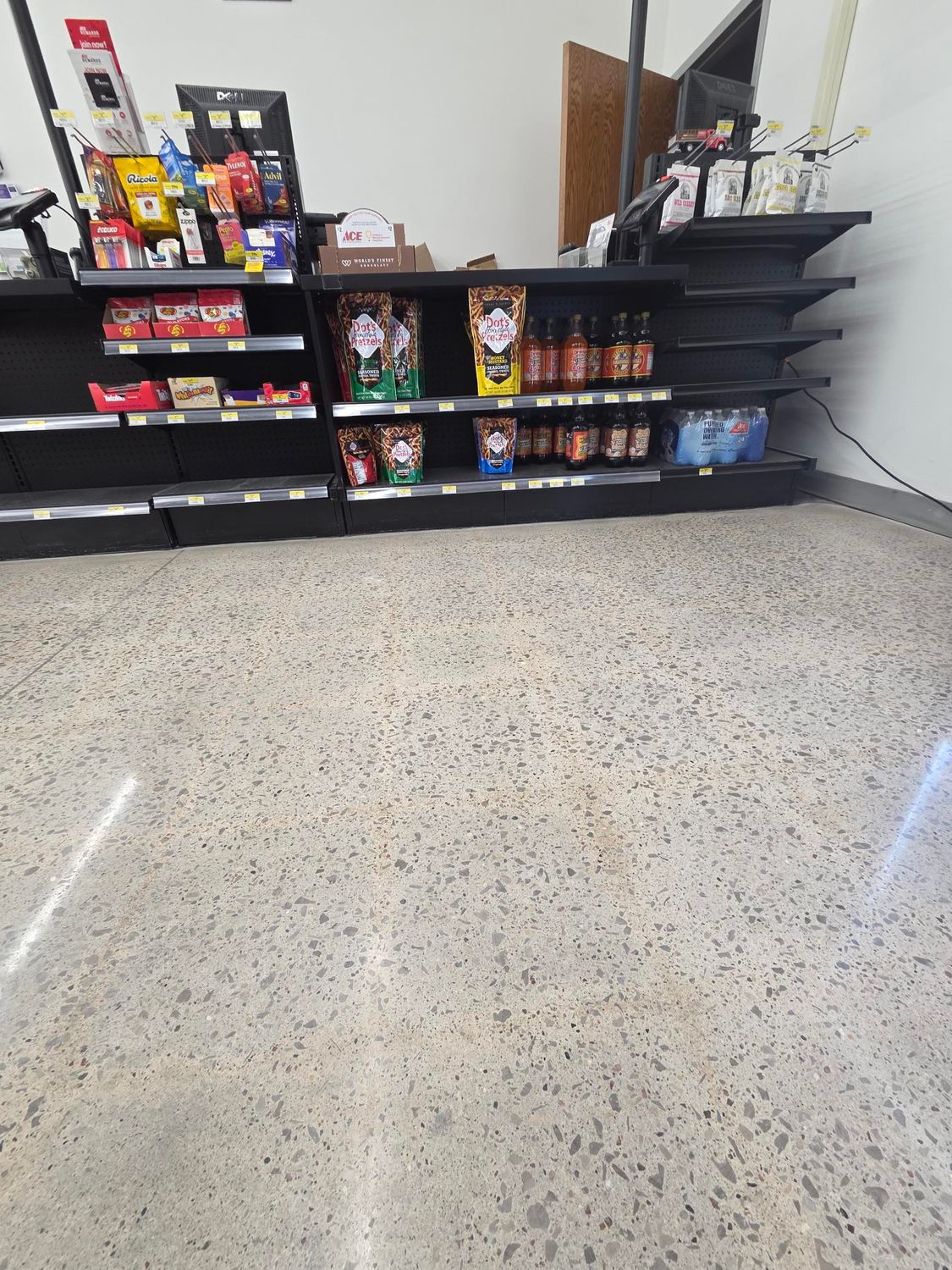 A retail checkout counter with black shelving stocked with various snack items, set against a light-colored terrazzo floor