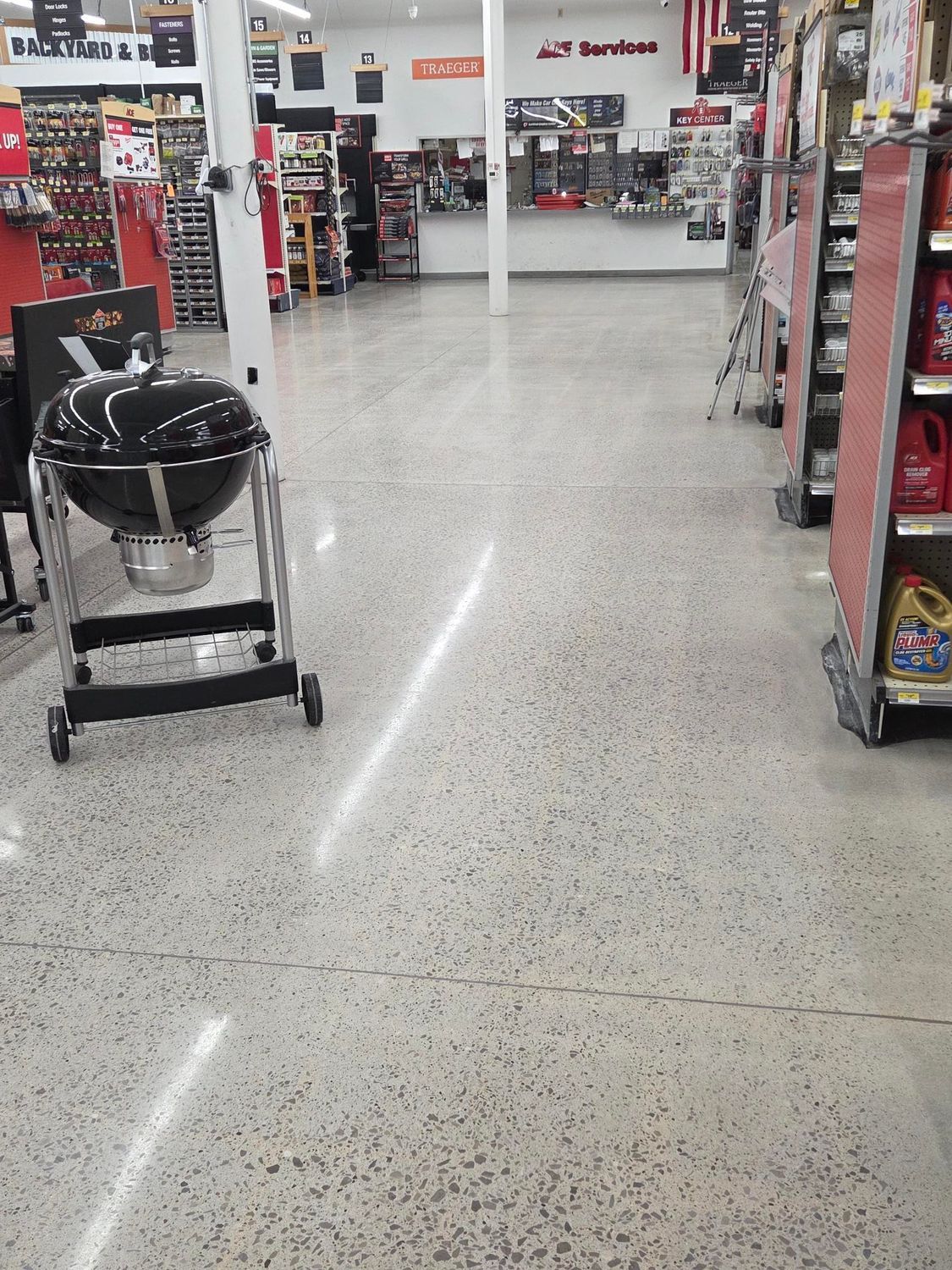 A black grill on wheels sits on a shiny, speckled concrete floor in the aisle of a hardware or home improvement store