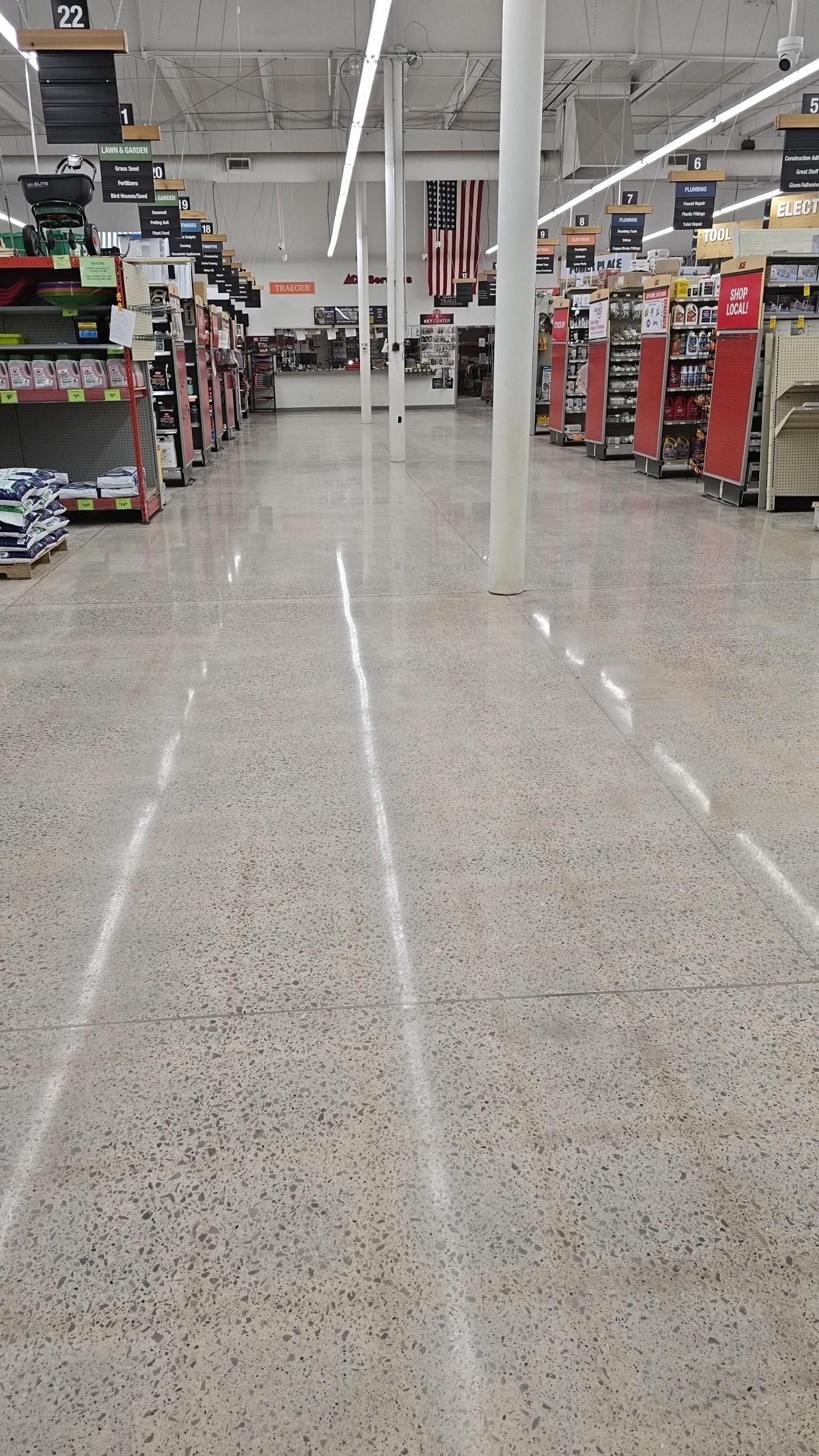 A view down a brightly lit retail store aisle with polished speckled flooring, white support pillars, and metal shelving