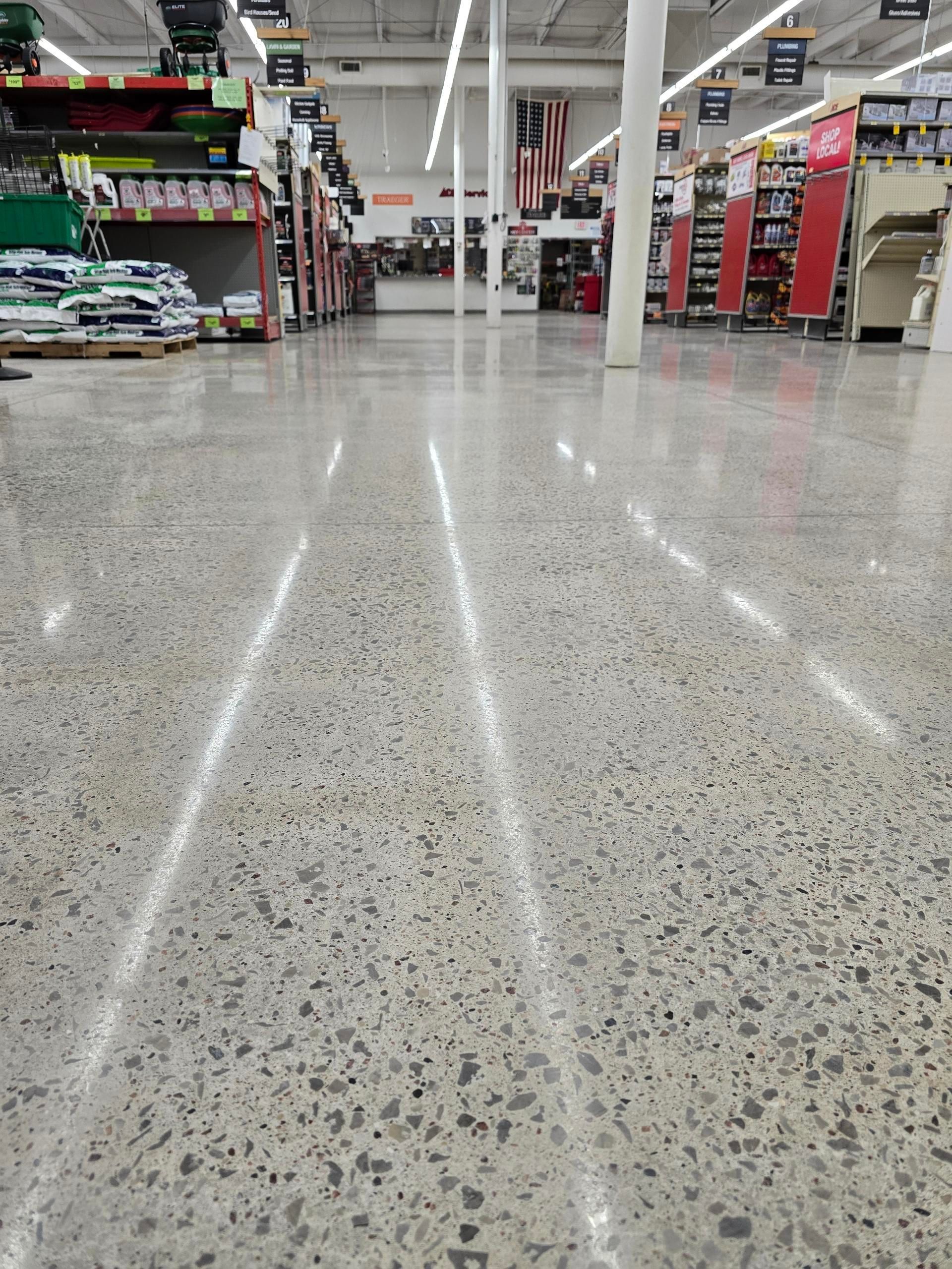 A low-angle view looking down the polished, speckled concrete aisle of a brightly lit hardware store