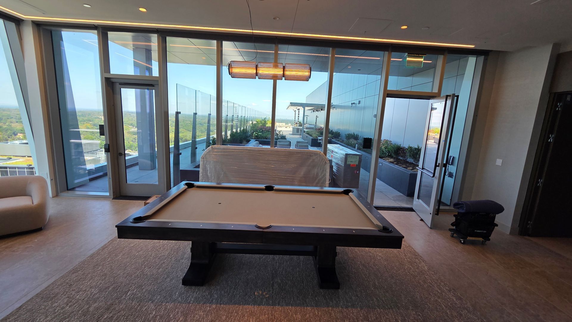A modern, light-filled lounge featuring a billiards table on a rug, positioned in front of floor-to-ceiling balcony doors.