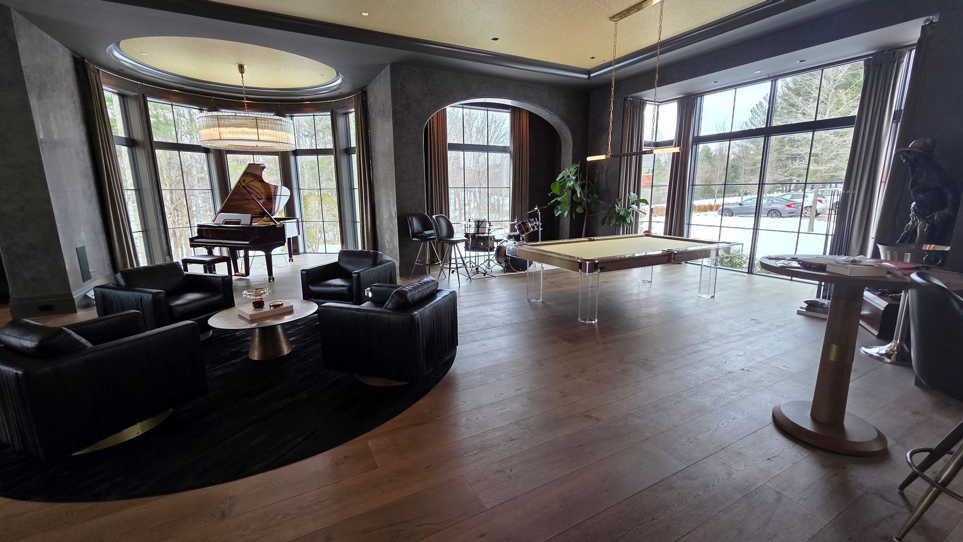 A spacious, modern room with a black seating area, a grand piano, a large dining table, and floor-to-ceiling windows.