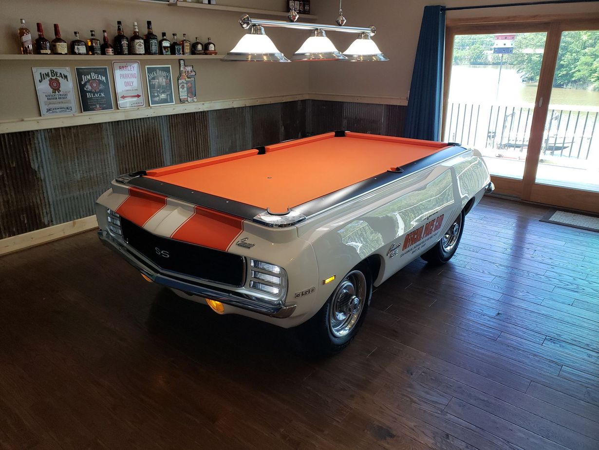 A pool table designed to look like the front half of a white classic Chevrolet Camaro with orange racing stripes.