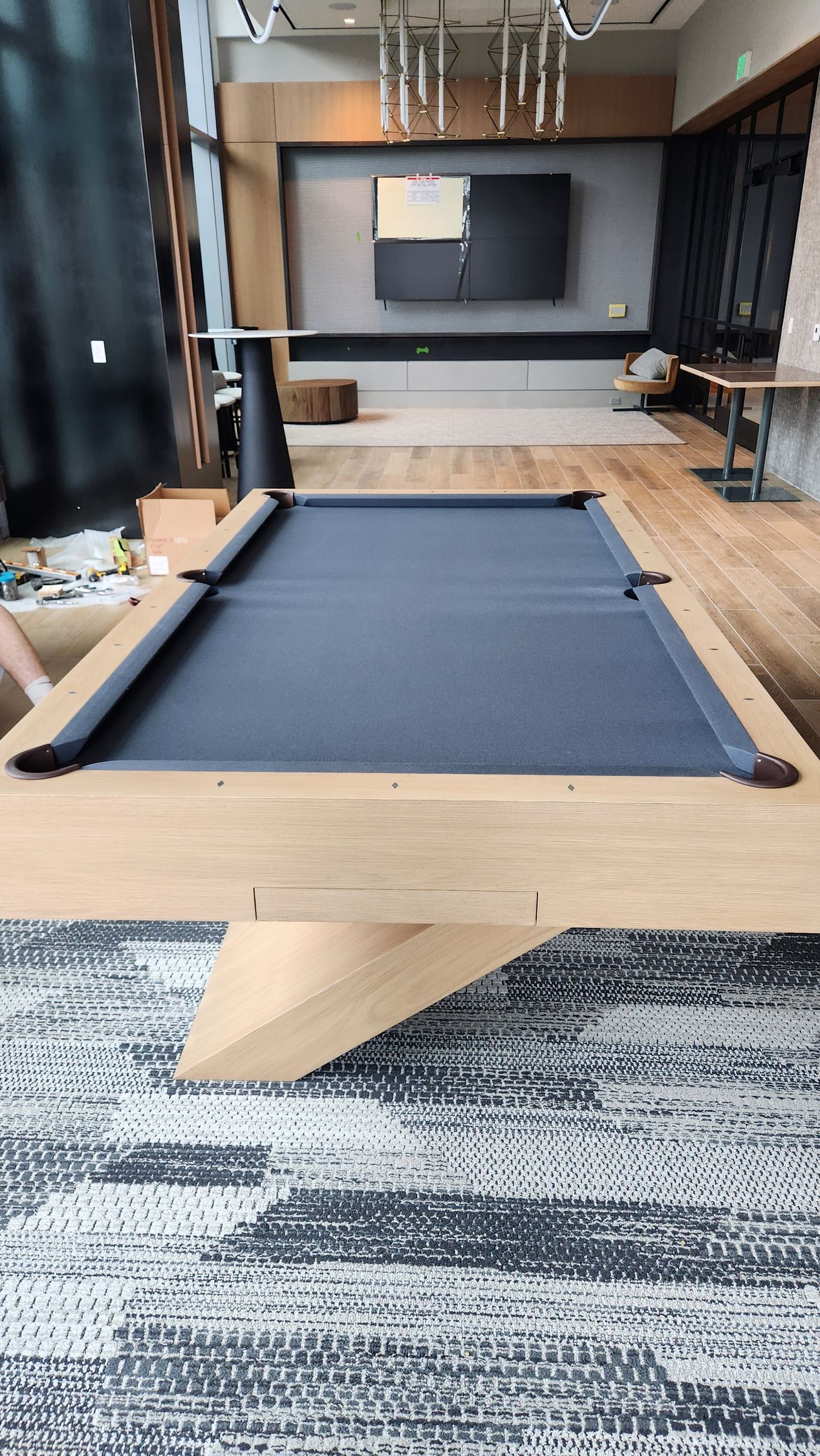A modern pool table with a gray felt surface sits in a contemporary lounge area with wood floors and a patterned rug.