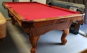 A set of seven translucent red polyhedral dice filled with gold flakes, arranged on a dark, textured surface.
