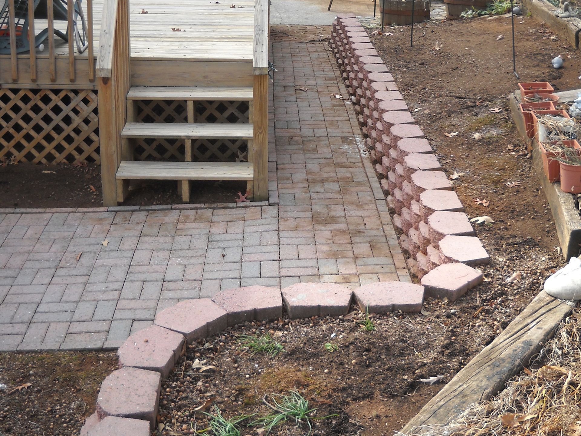 Brick pathway leading to wooden stairs, bordered by a retaining wall and garden edging.