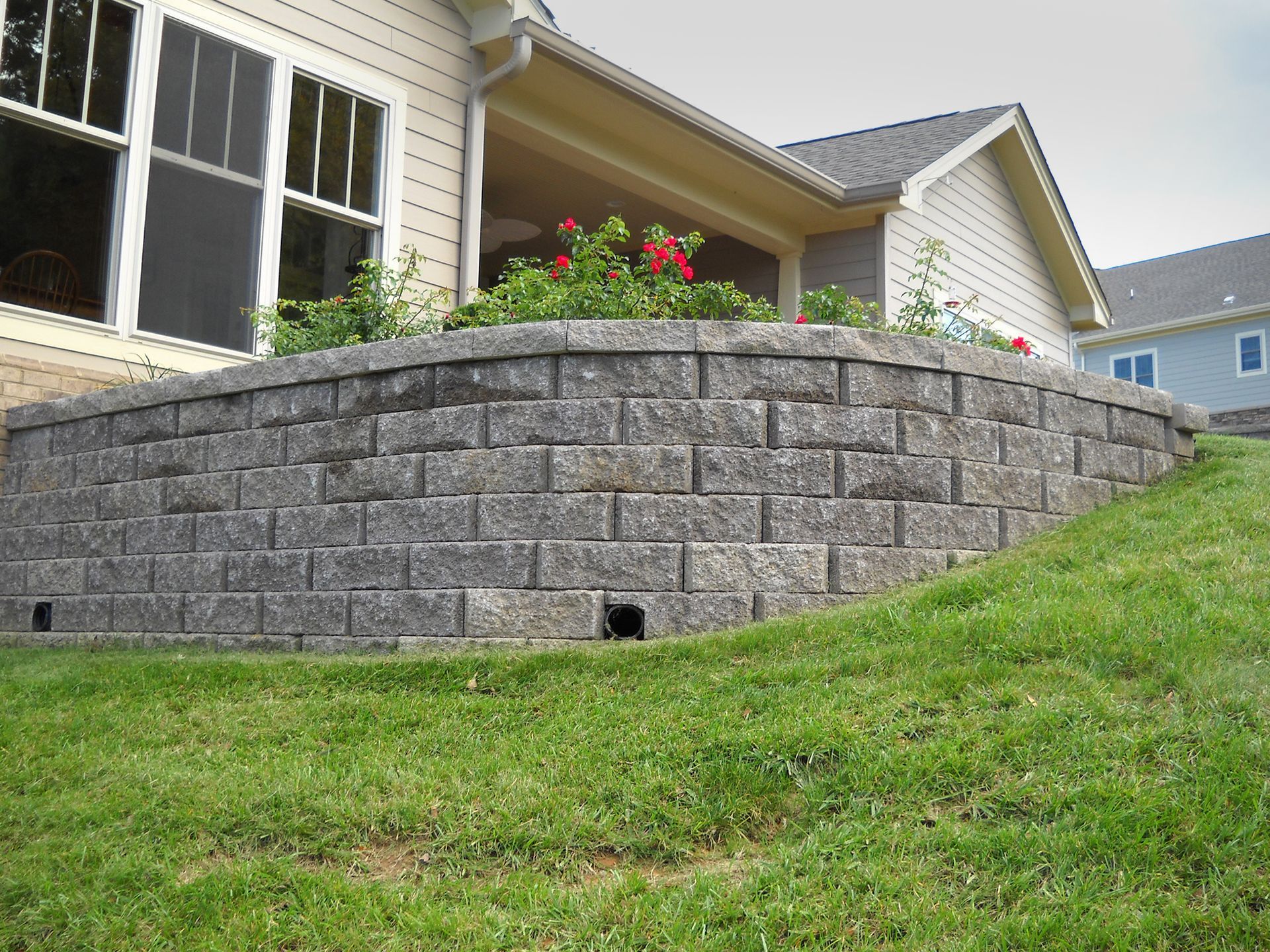 Stone retaining wall with a planted garden bed next to a house with a green lawn.
