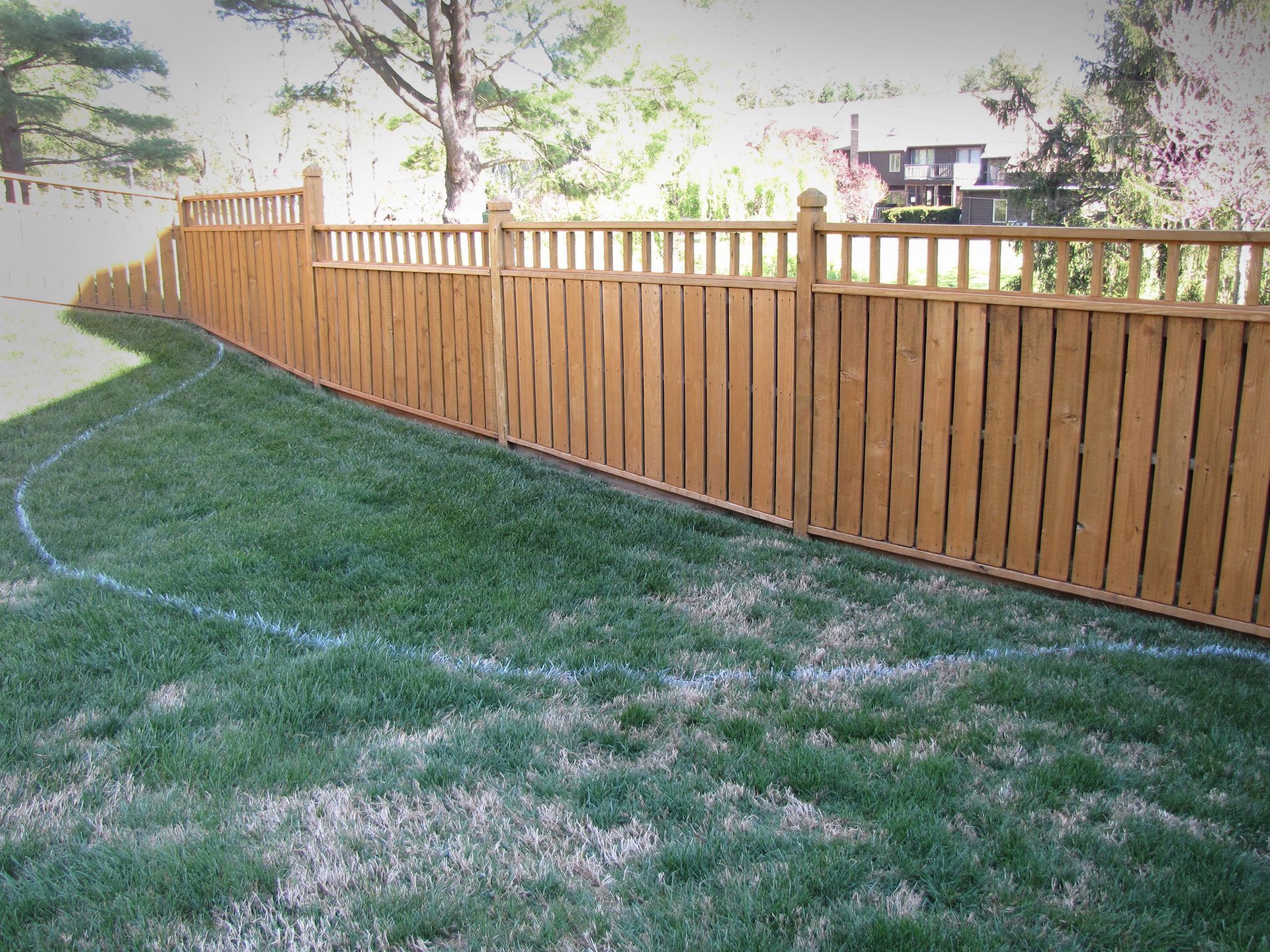 Wooden fence in a yard with green grass, following a curved line marked on the ground.
