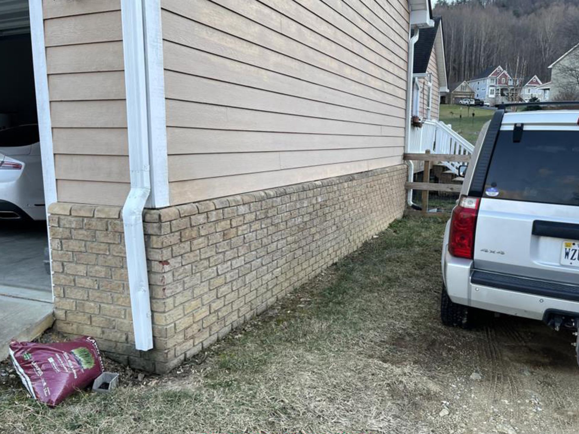 Garage exterior with light tan siding over brick, white SUV parked nearby.