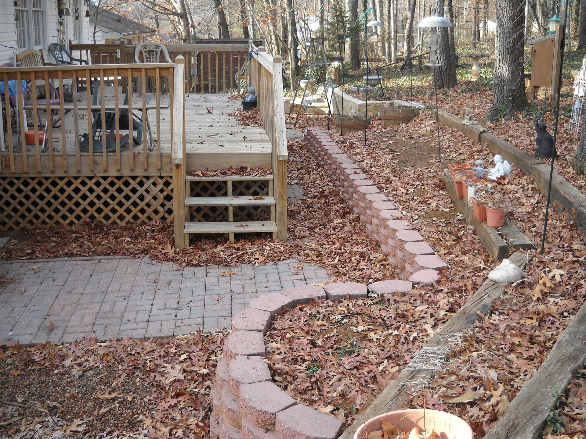 A brick path winds through a yard with a wooden deck and fallen leaves.