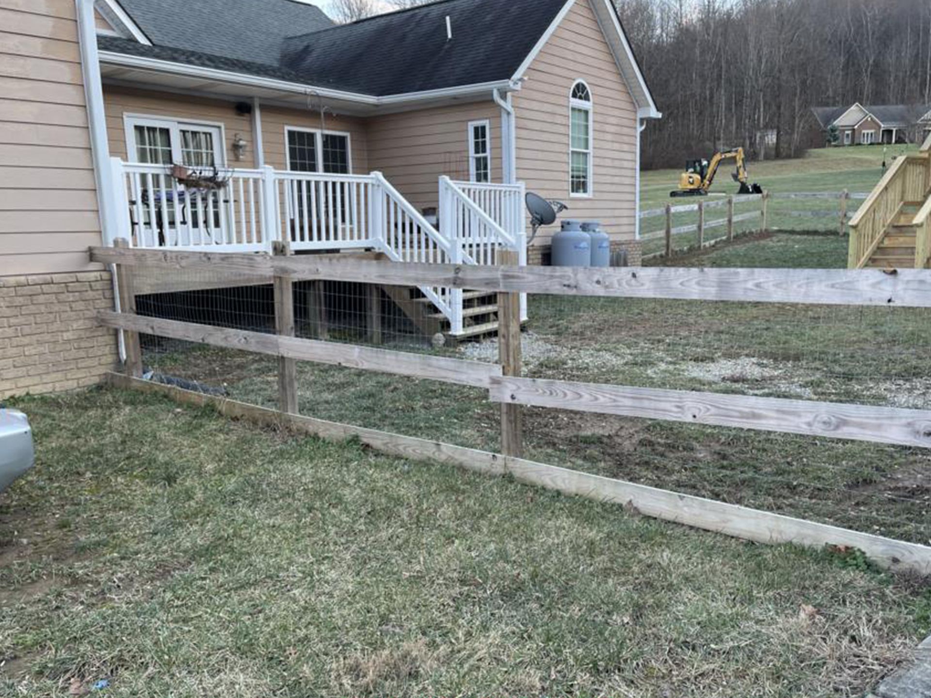 Backyard with a wooden fence, deck, and house. An excavator is in the distance.