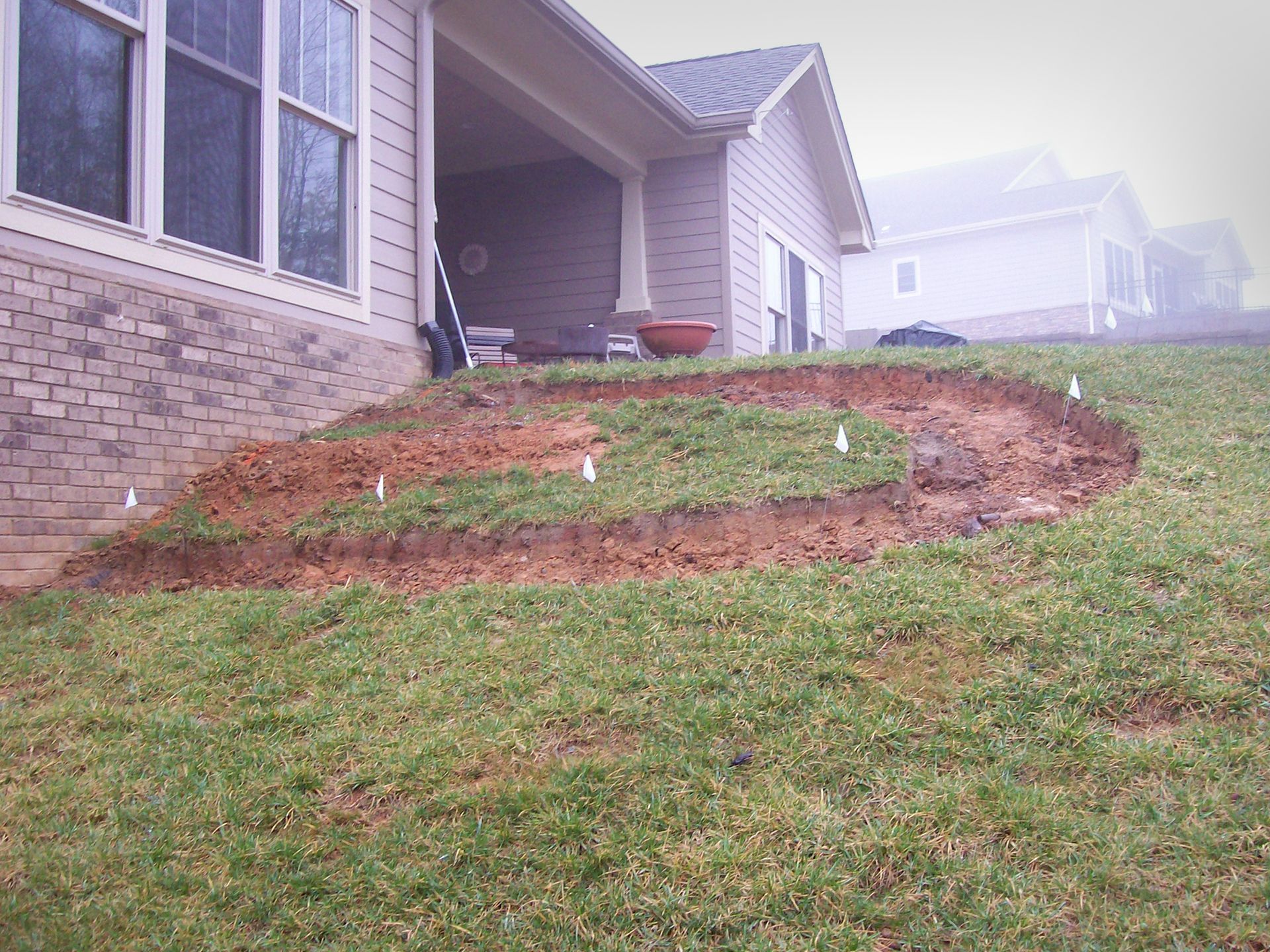 Excavated garden bed on a sloped lawn next to a house. Markers delineate the bed's circular shape.