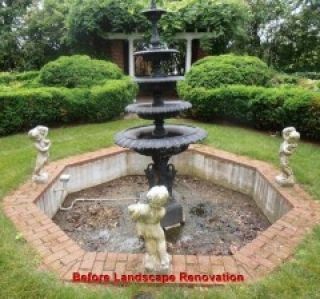 A tiered fountain in an octagonal brick-lined basin, surrounded by manicured shrubs. Two statues flank the fountain.
