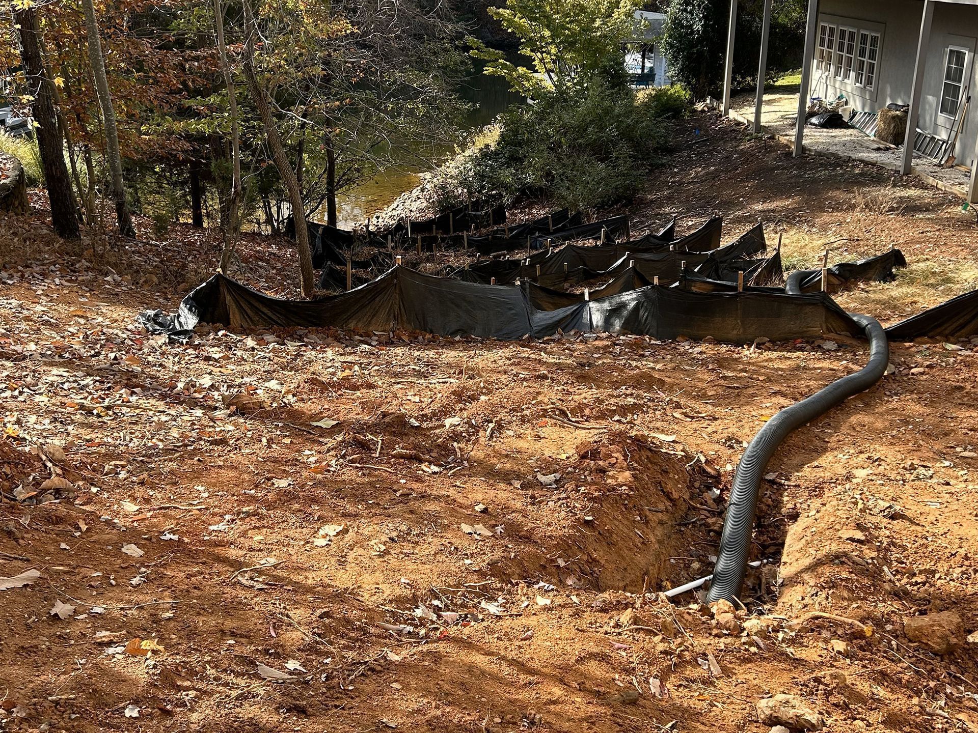 Erosion control fabric on a hillside with a drainage pipe, surrounded by leaves and dirt.