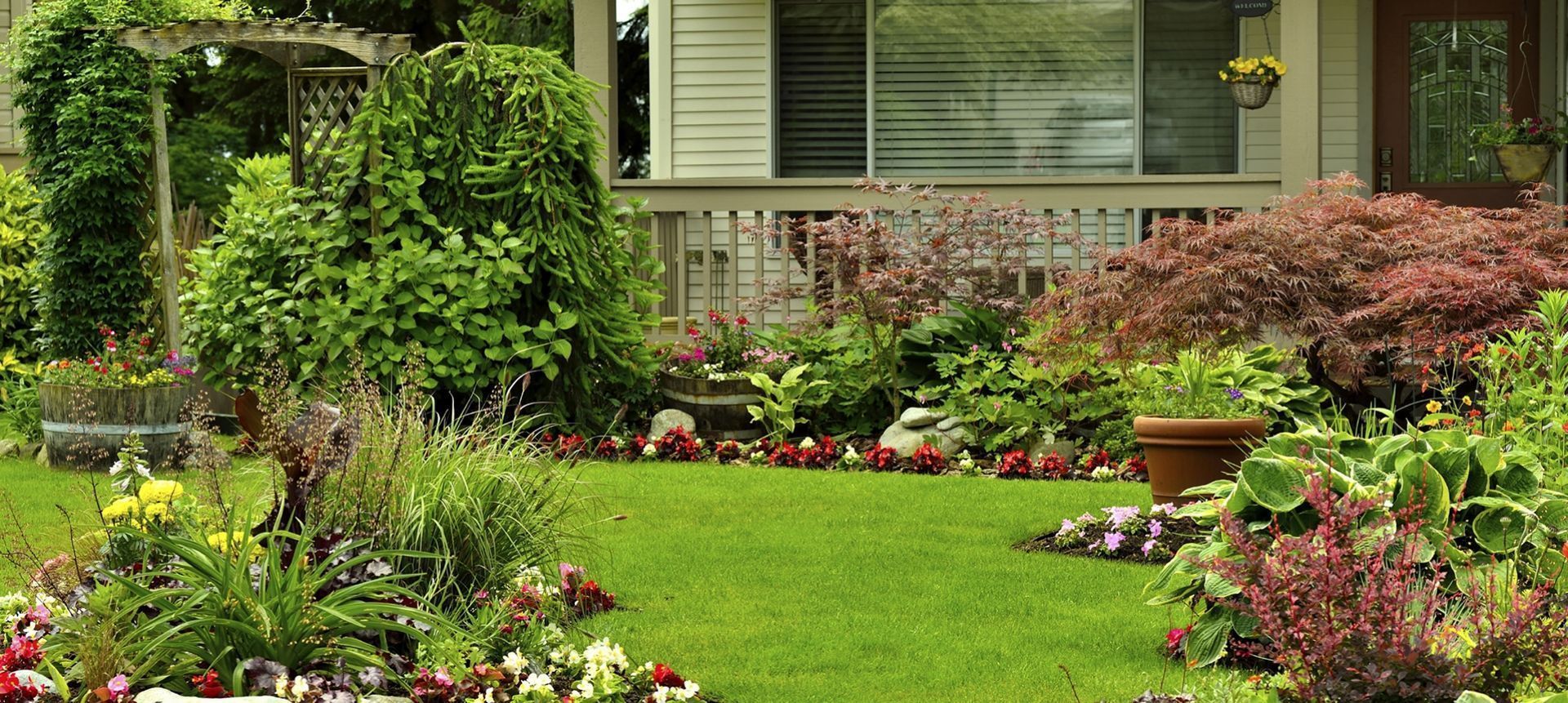 Lush front yard with green grass, flowers, and bushes, in front of a house.