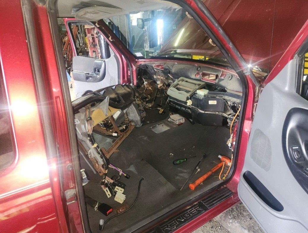 Interior of a red pickup truck with the dashboard and components removed, exposed wiring.