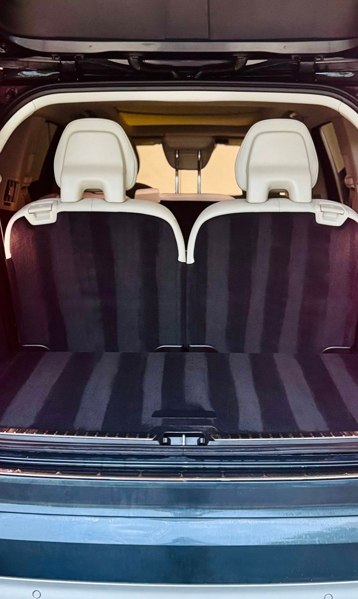 Car trunk interior with two beige headrests. Dark interior, striped black and dark carpet, open tailgate.