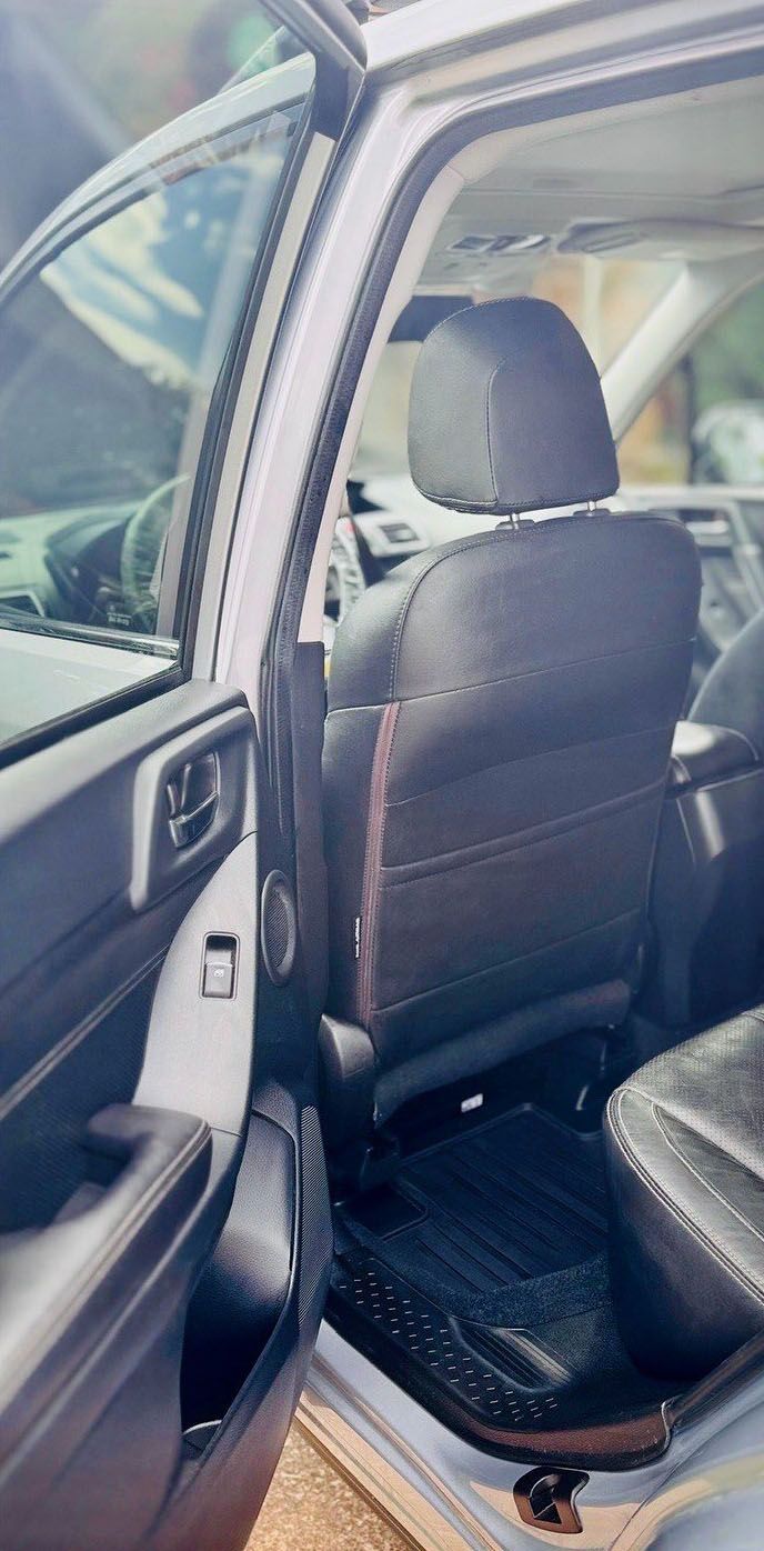 Interior of a car. Black leather seats, door, and floor mat. Open door. Sunlight.