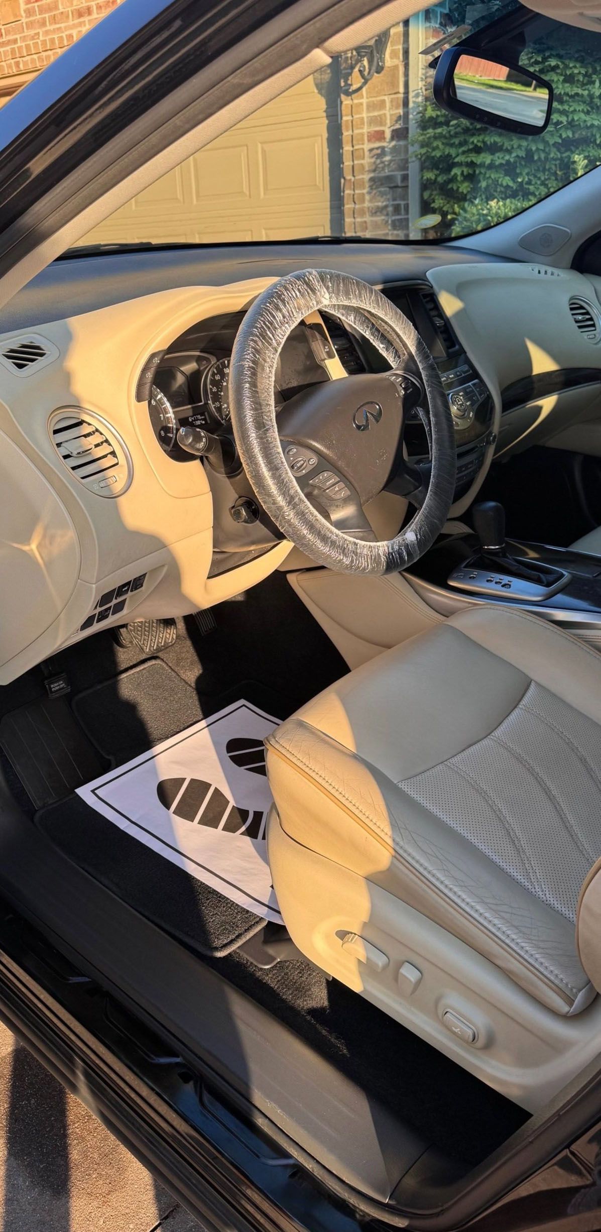 Interior of a tan car. Steering wheel wrapped in clear plastic. Tan dashboard and seats. Black floor mats.