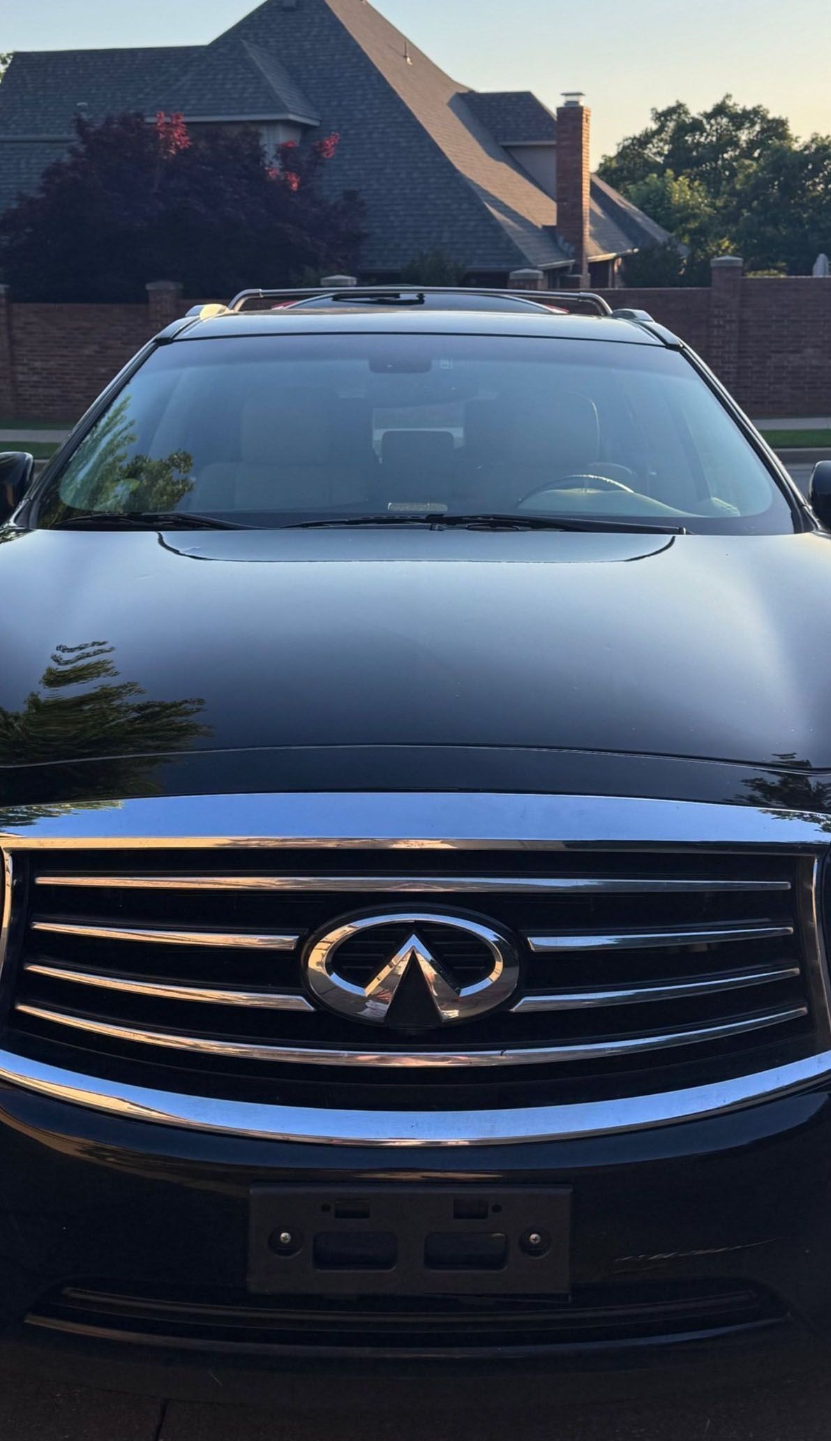 Black Infiniti SUV, front view, shiny grill, emblem, parked outside a house.