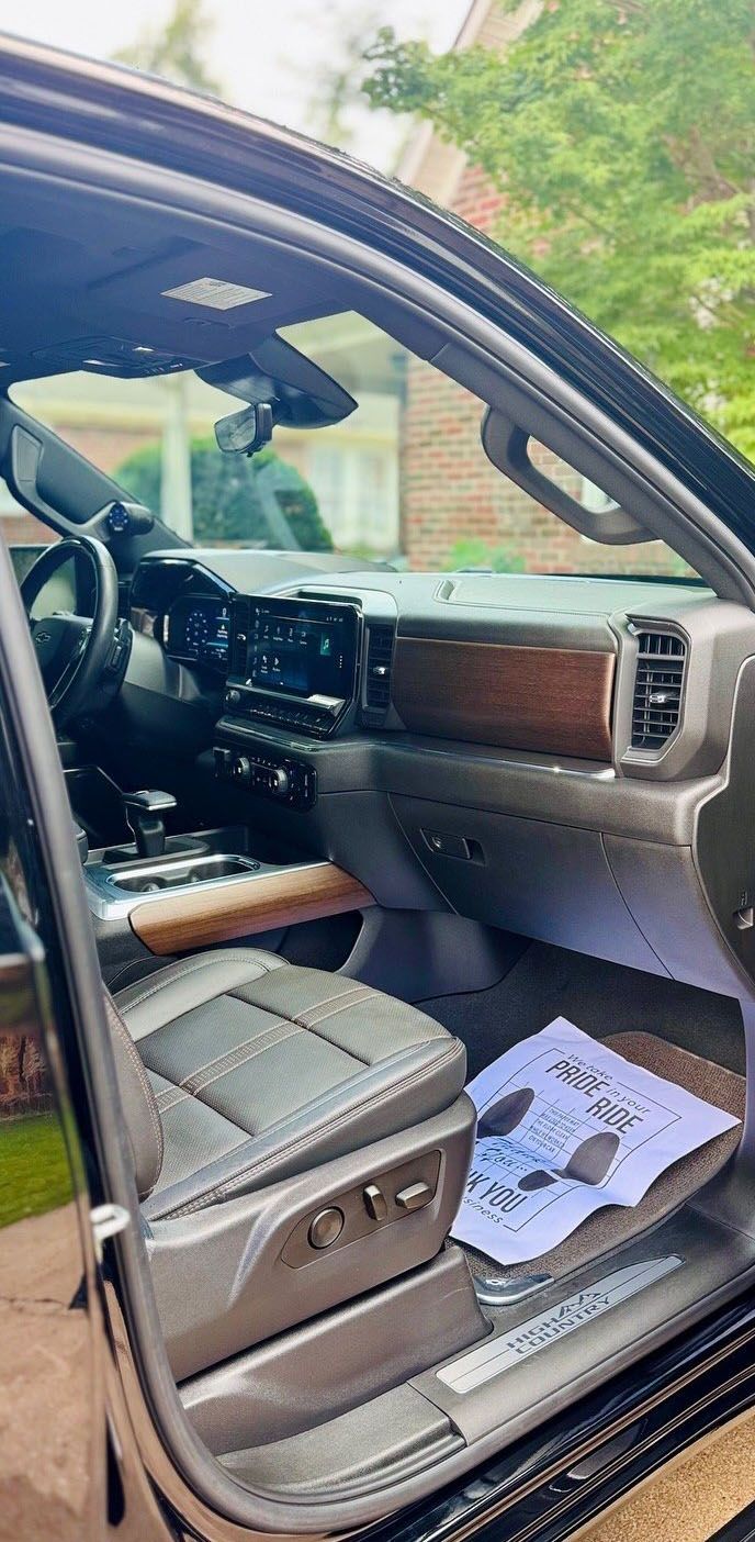 Interior view of a dark truck with a wood-trimmed dashboard, black seats, and a paper with keys on the floor.