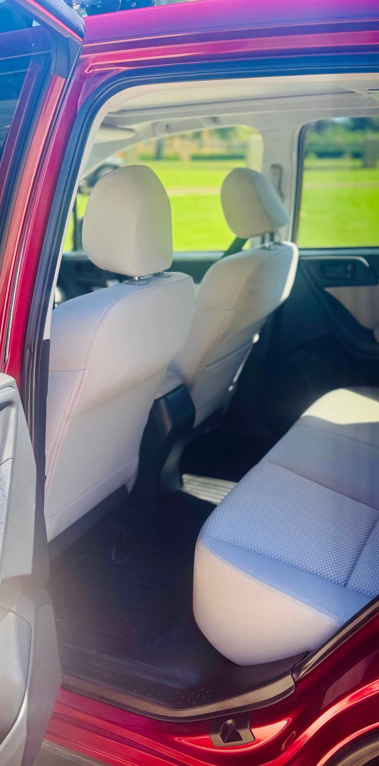 Interior of a red car with light-colored seats, featuring the back row.
