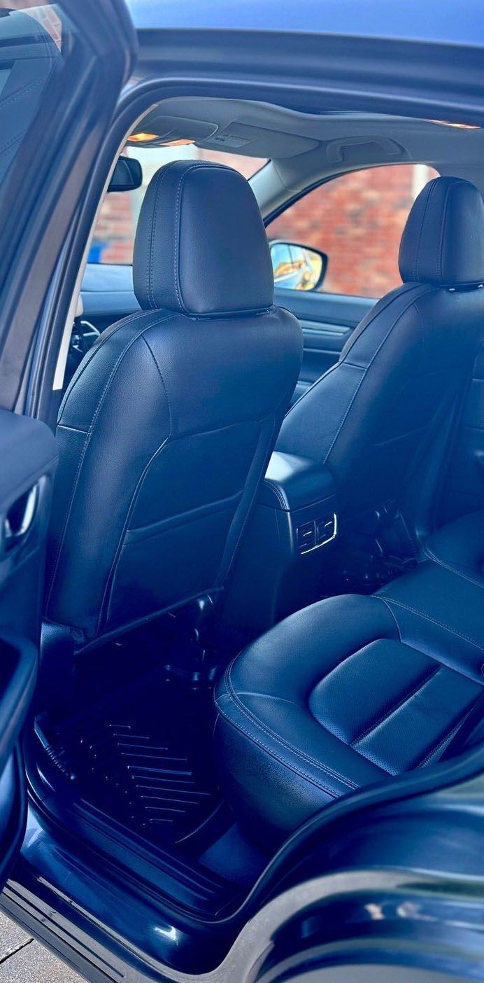 Interior view of a dark blue car. Focus on the leather seats in the backseat with black floor mats.