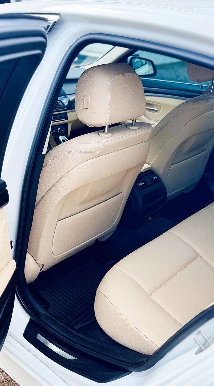 Beige leather interior of a white car, showing rear seats, headrests, and door.