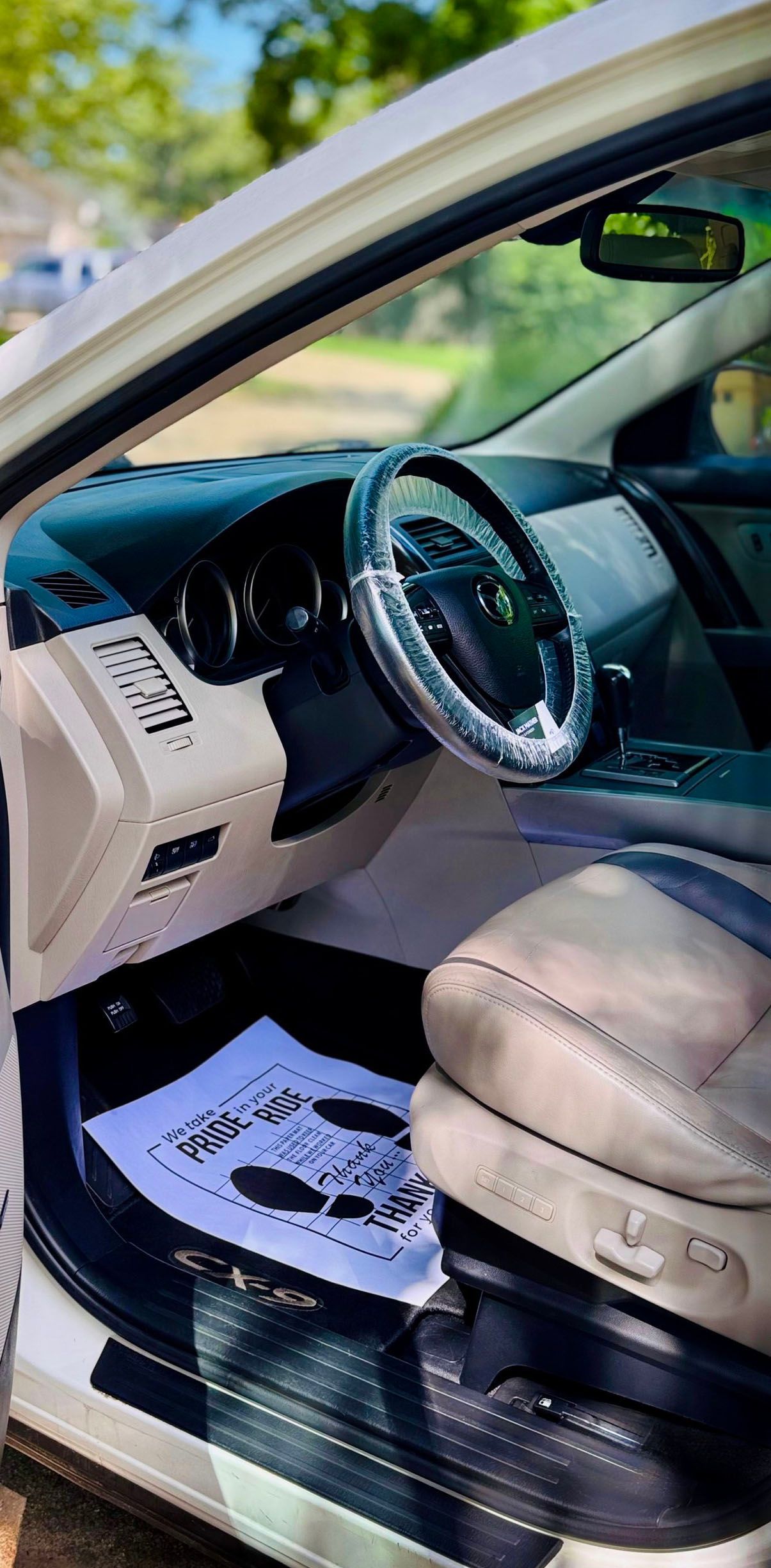 Interior of a white car, featuring a steering wheel, beige dashboard and front seat, and a paper on the floor.