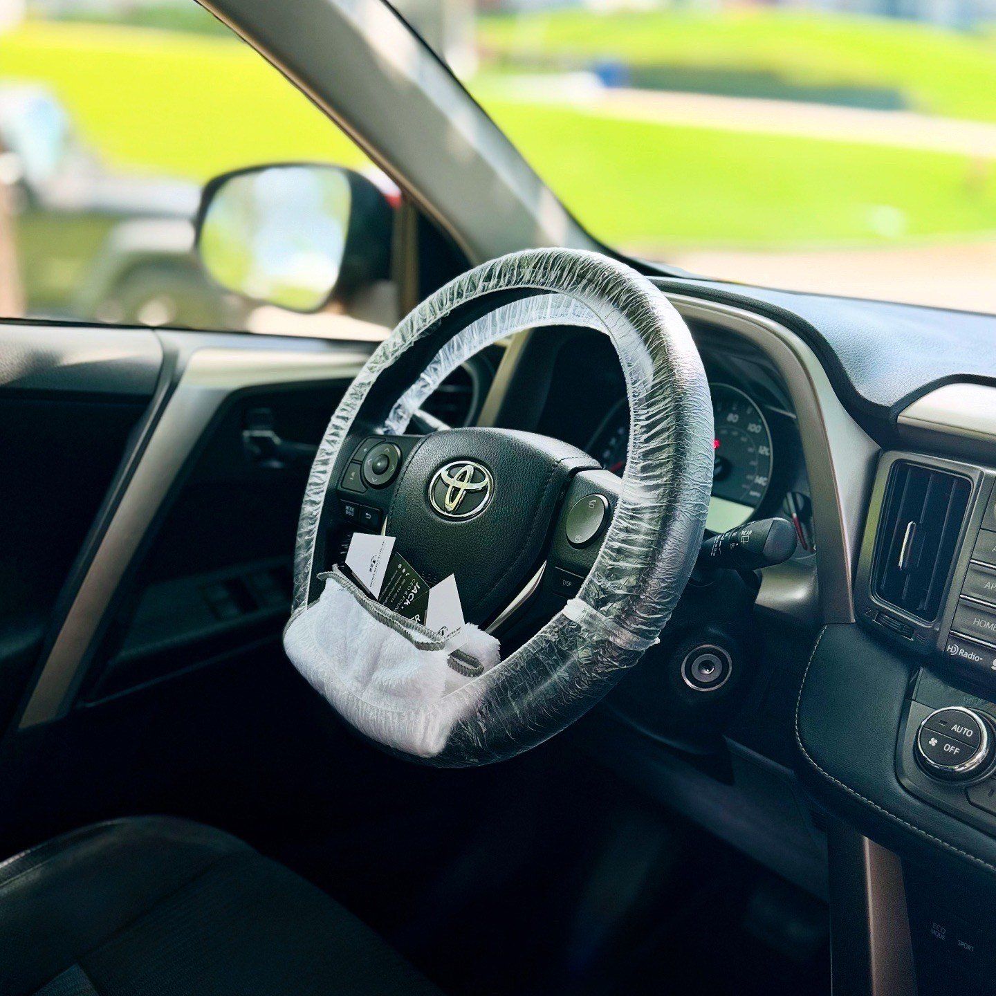 Interior of a Toyota RAV4 with a steering wheel covered in plastic and a cloth on the side.