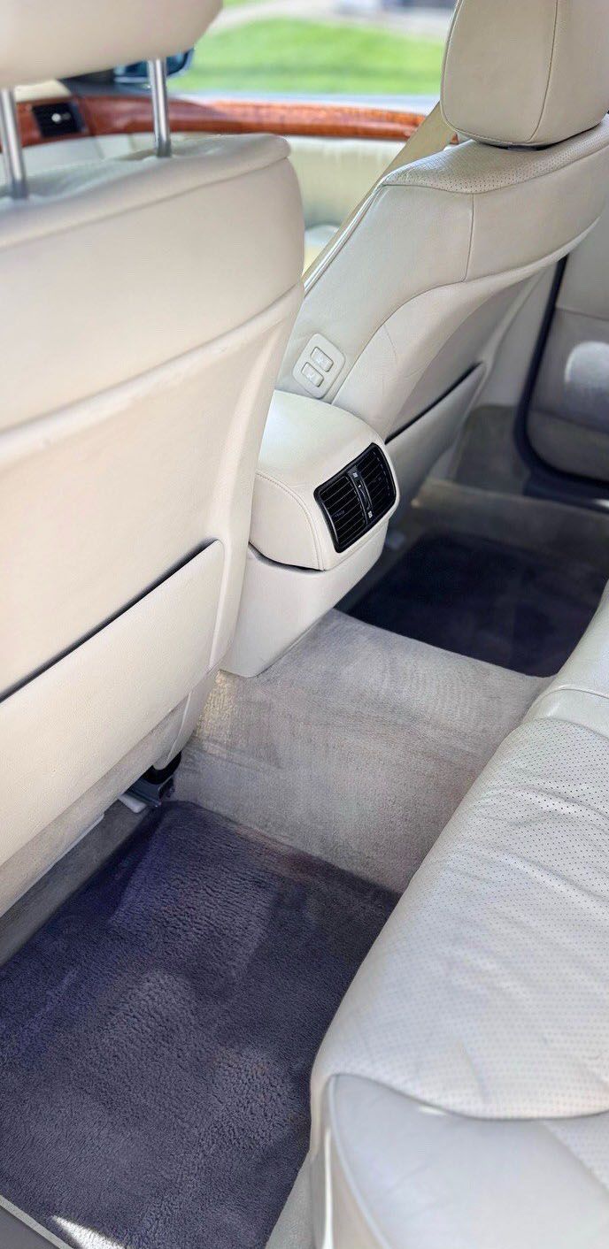 Interior view of a car's backseat with cream-colored leather seats and dark gray carpeting.